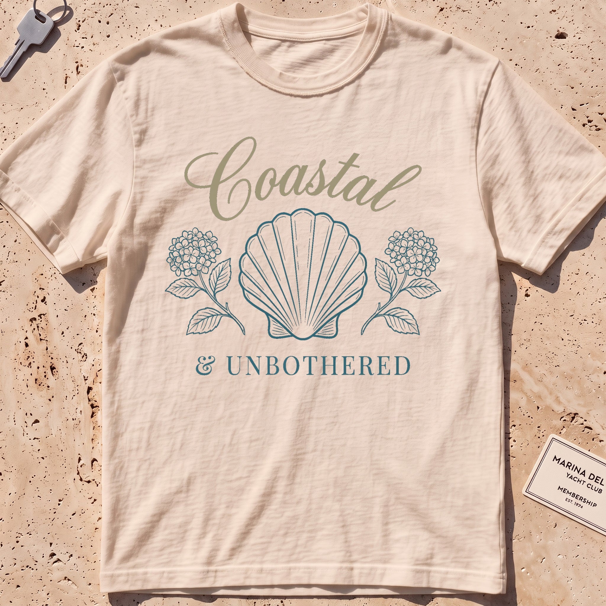 ivory heavyweight tee with a shell and hydrangea "Coastal and Unbothered" graphic.