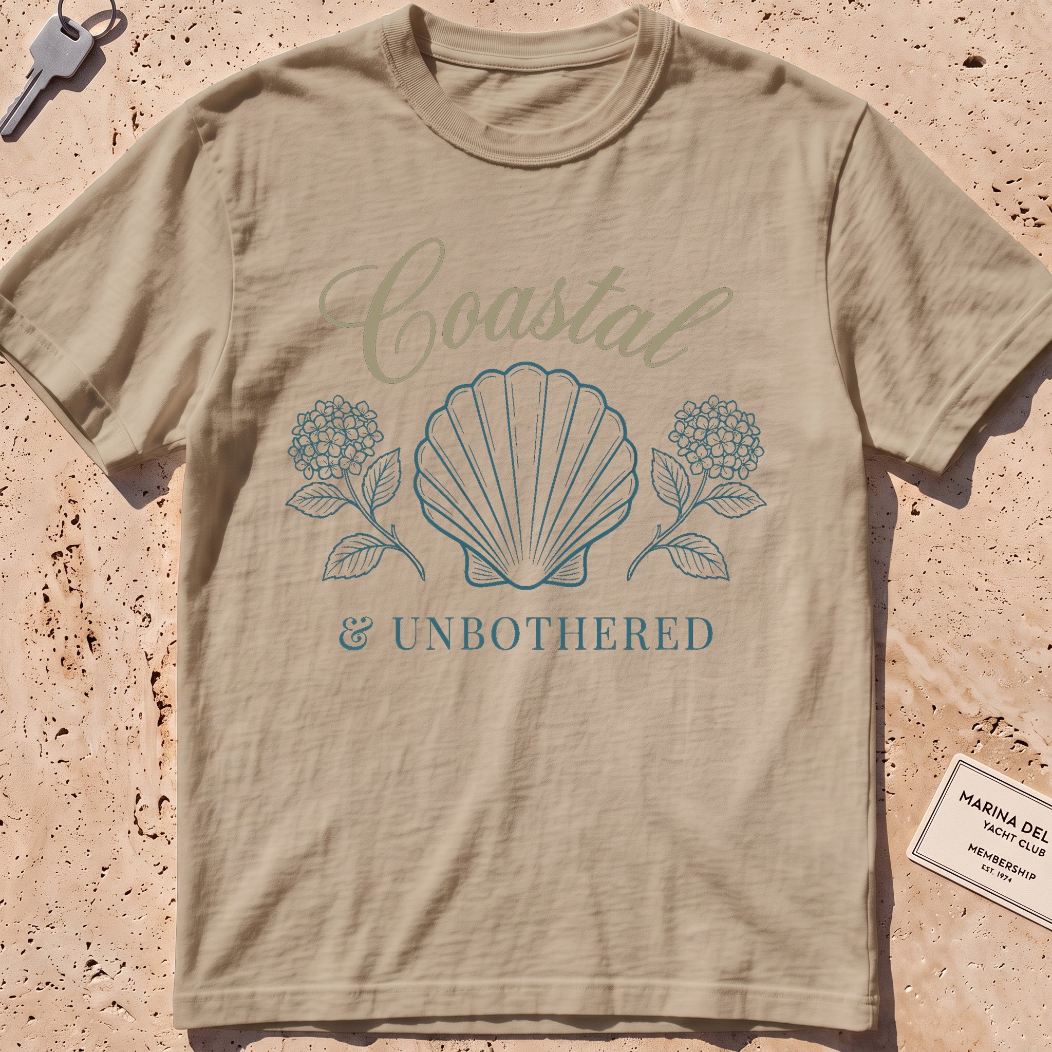 khaki heavyweight tee with a shell and hydrangea "Coastal and Unbothered" graphic.