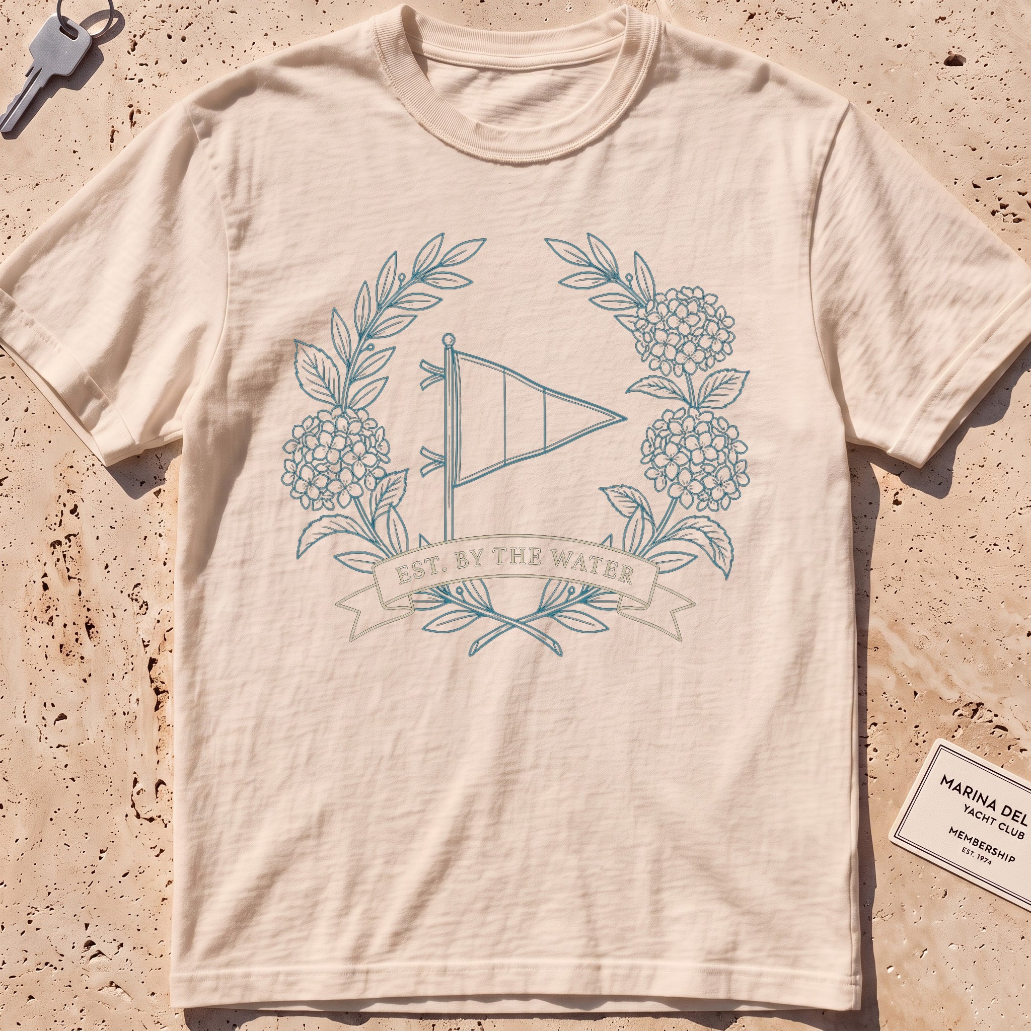 ivory heavyweight tee with a burgee and hydrangea wreath "Est. by the Water" graphic.