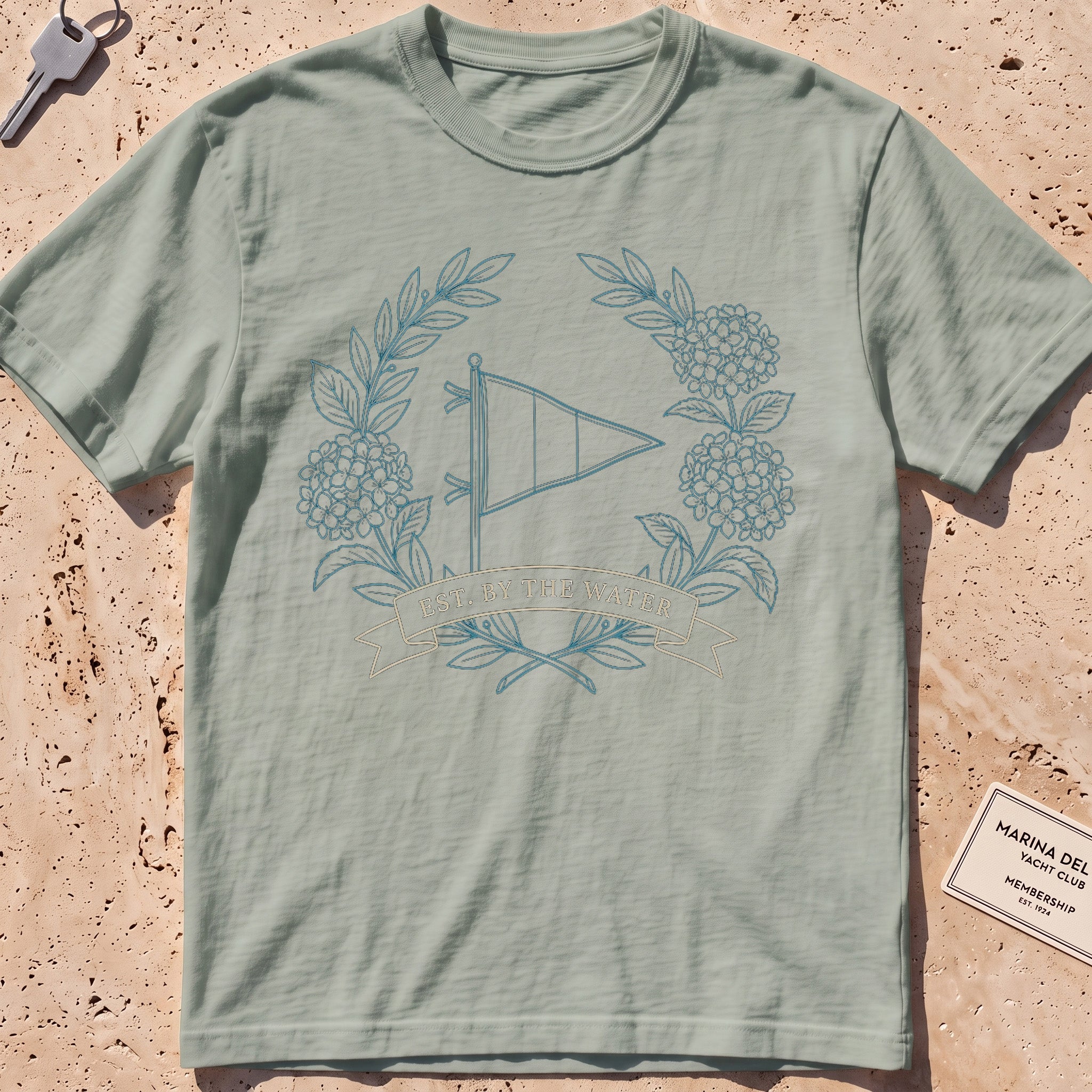 bay heavyweight tee with a burgee and hydrangea wreath "Est. by the Water" graphic.