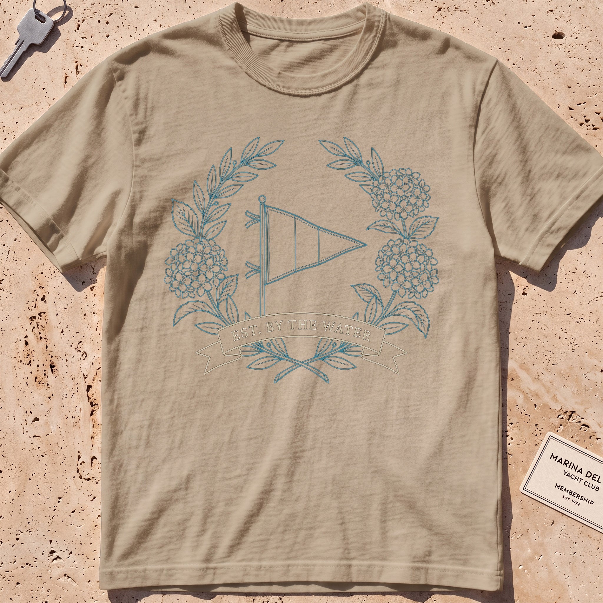 khaki heavyweight tee with a burgee and hydrangea wreath "Est. by the Water" graphic.