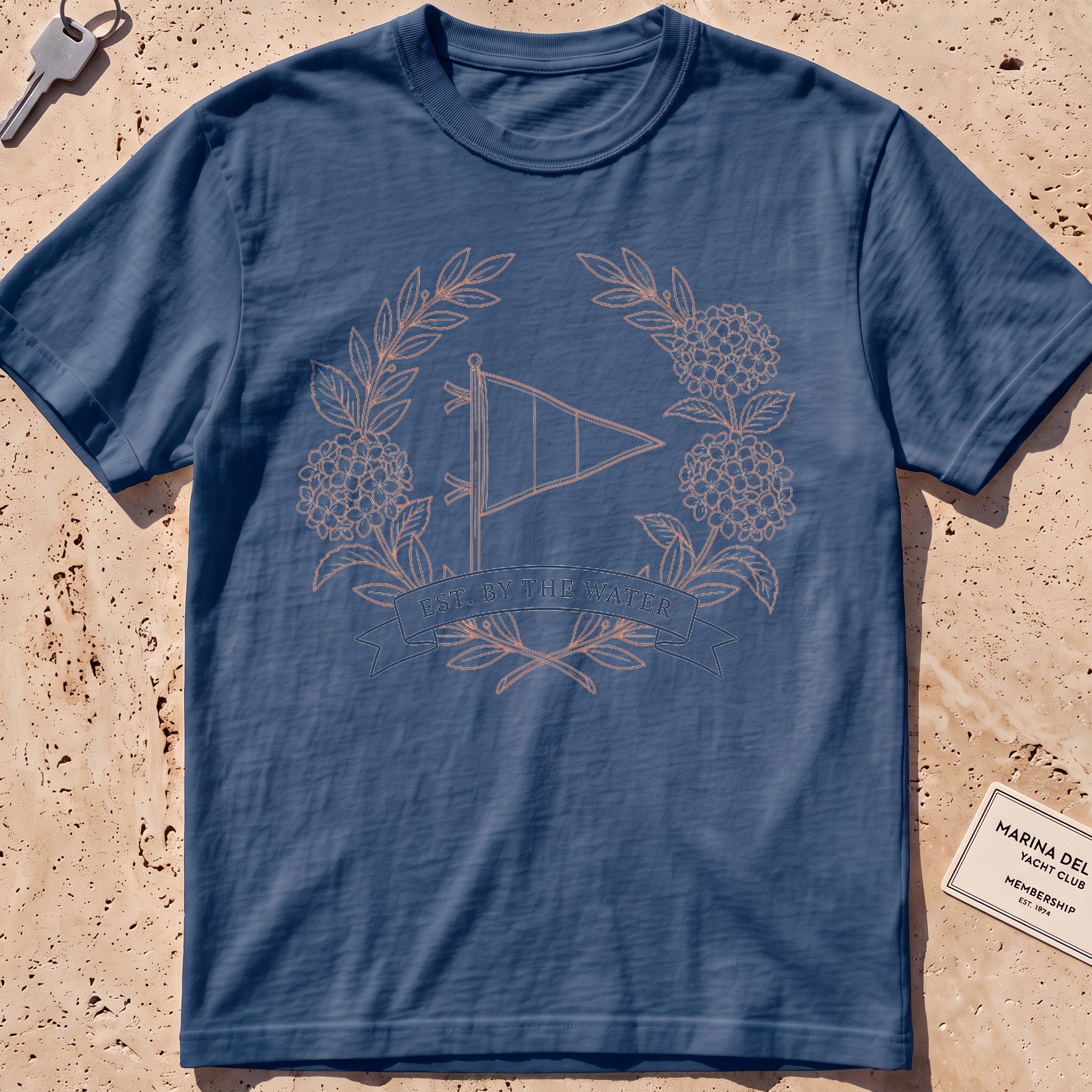 midnight heavyweight tee with a burgee and hydrangea wreath "Est. by the Water" graphic.