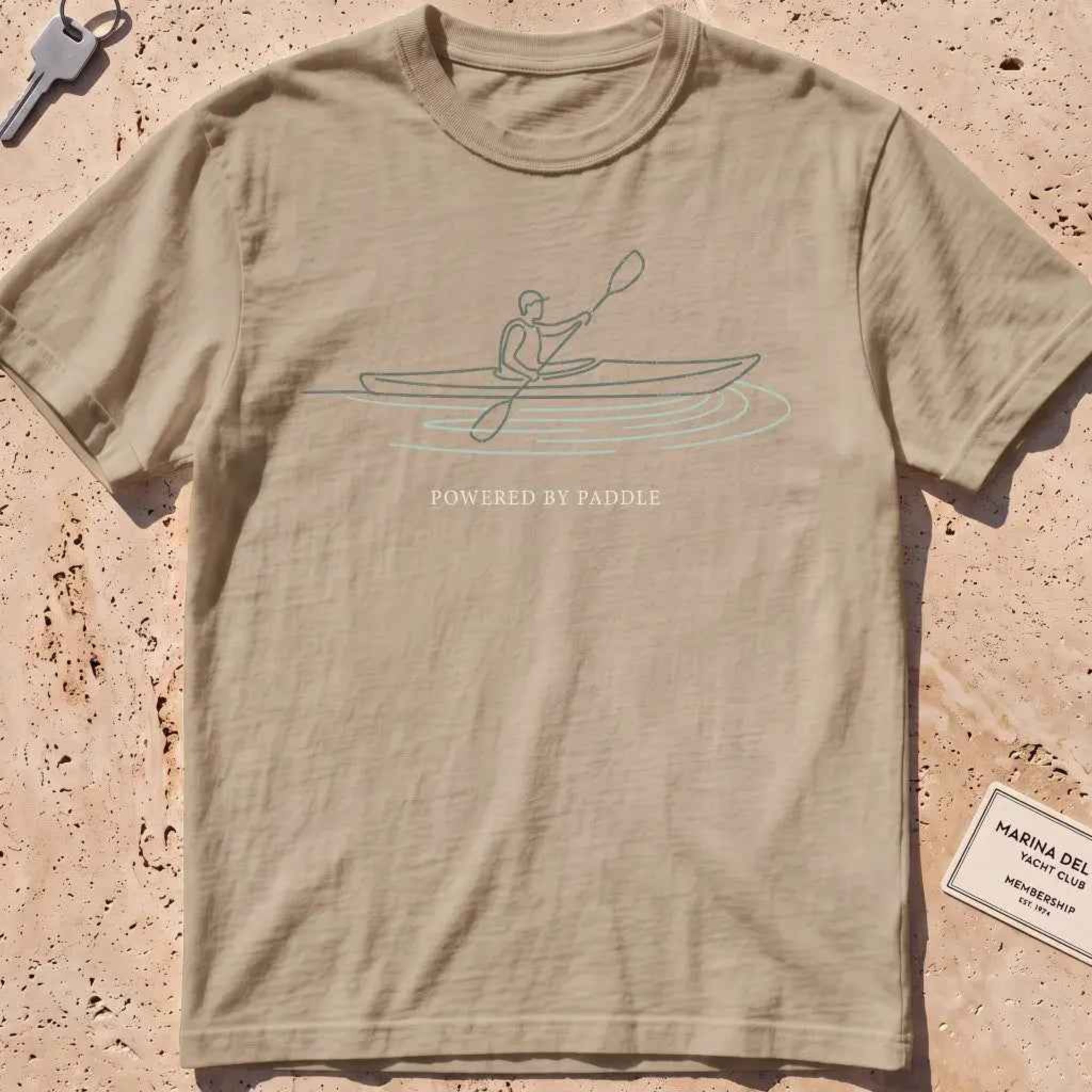 khaki heavyweight tee with a single-line kayaker "Powered by Paddle" graphic.