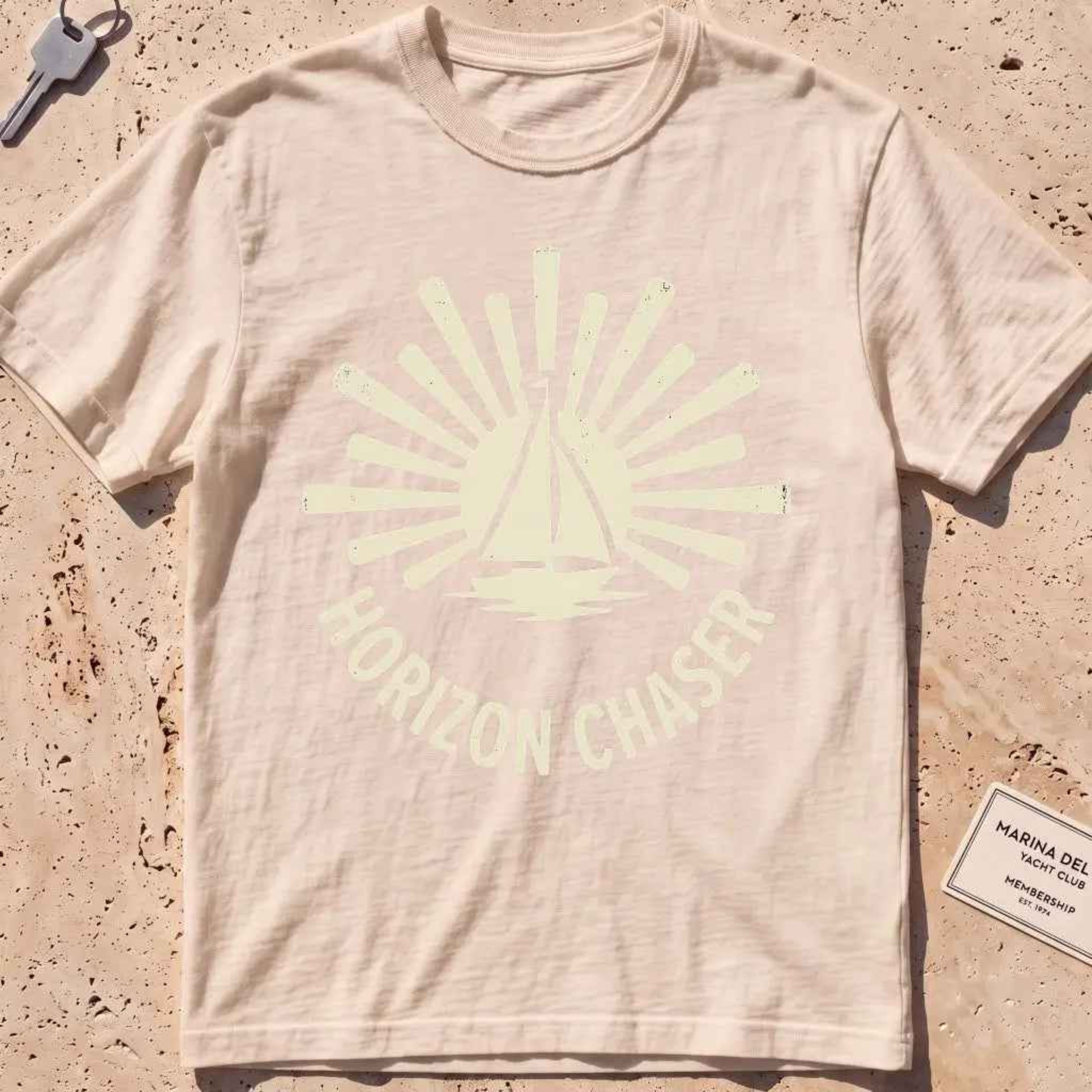 ivory heavyweight tee with a sunburst sailboat "Horizon Chaser" badge.
