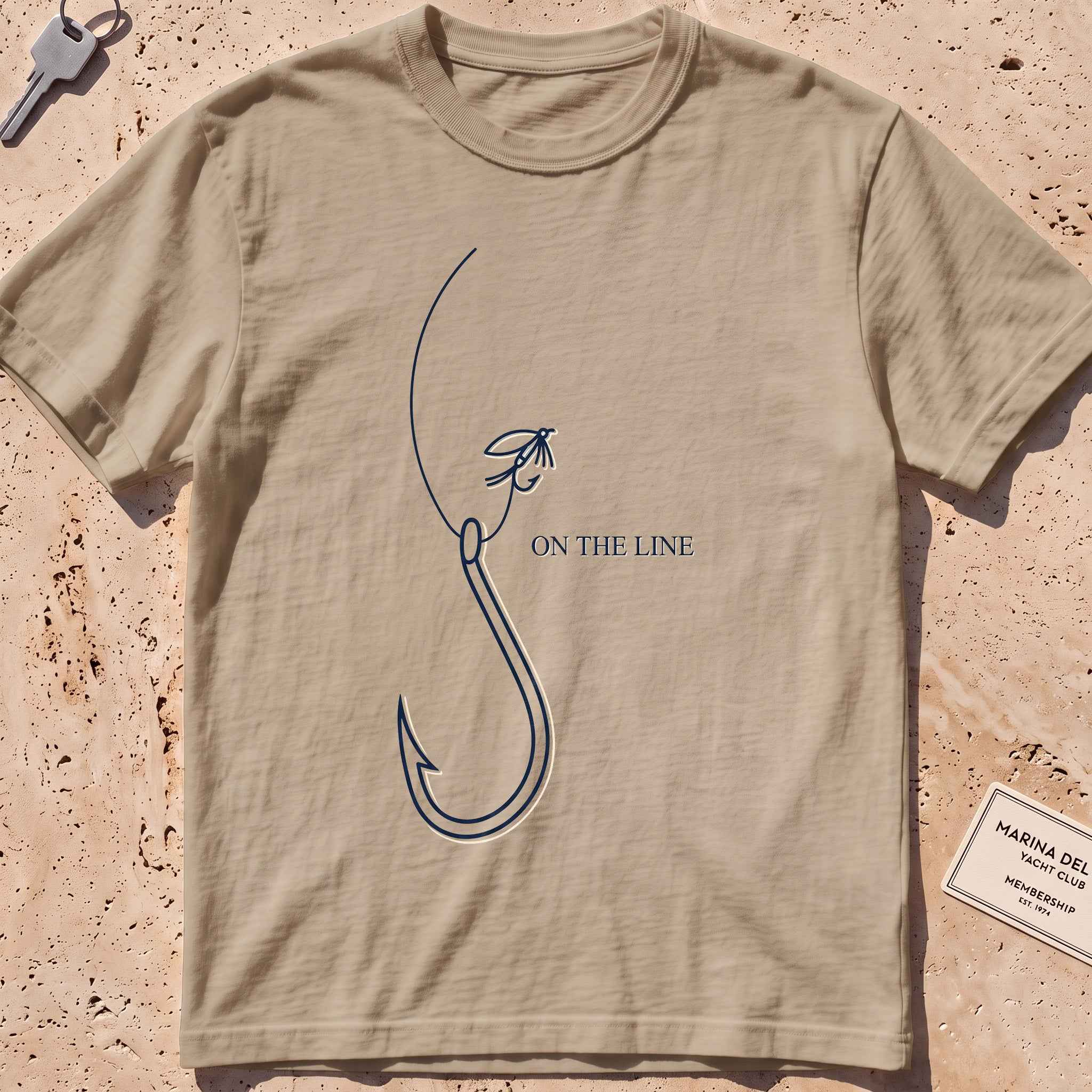 khaki heavyweight tee with a single-line fishing hook and fly graphic.