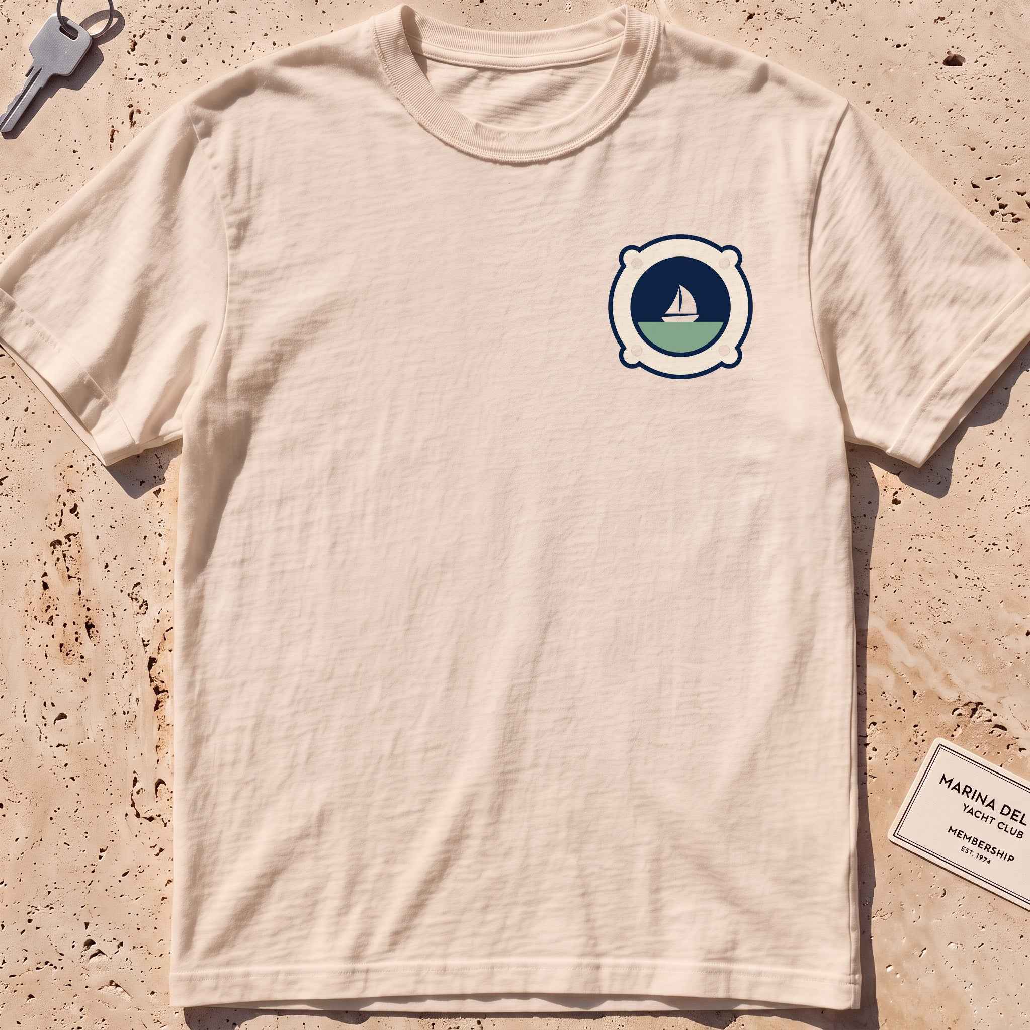 ivory heavyweight tee with a porthole framing a sailboat crest graphic.
