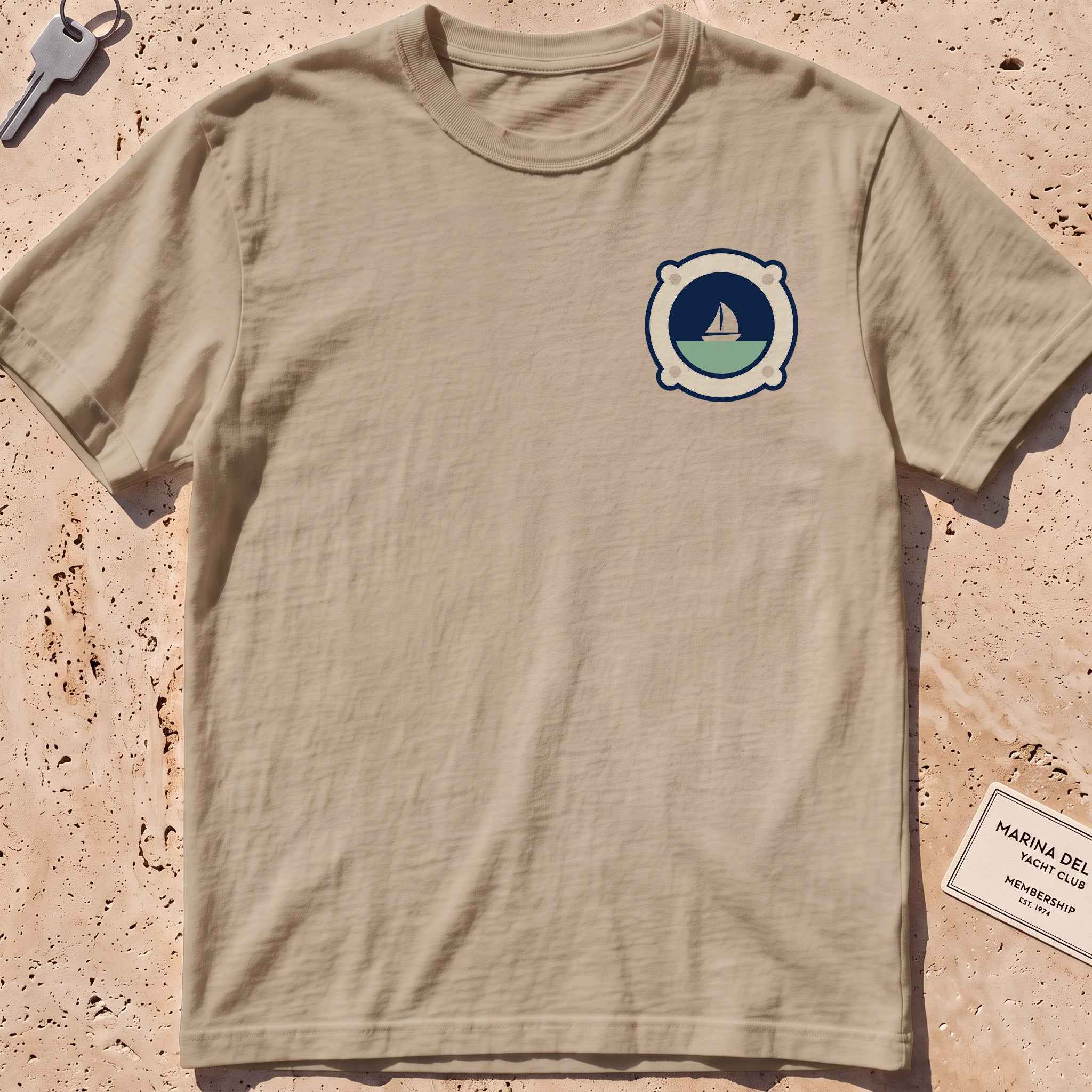 khaki heavyweight tee with a porthole framing a sailboat crest graphic.