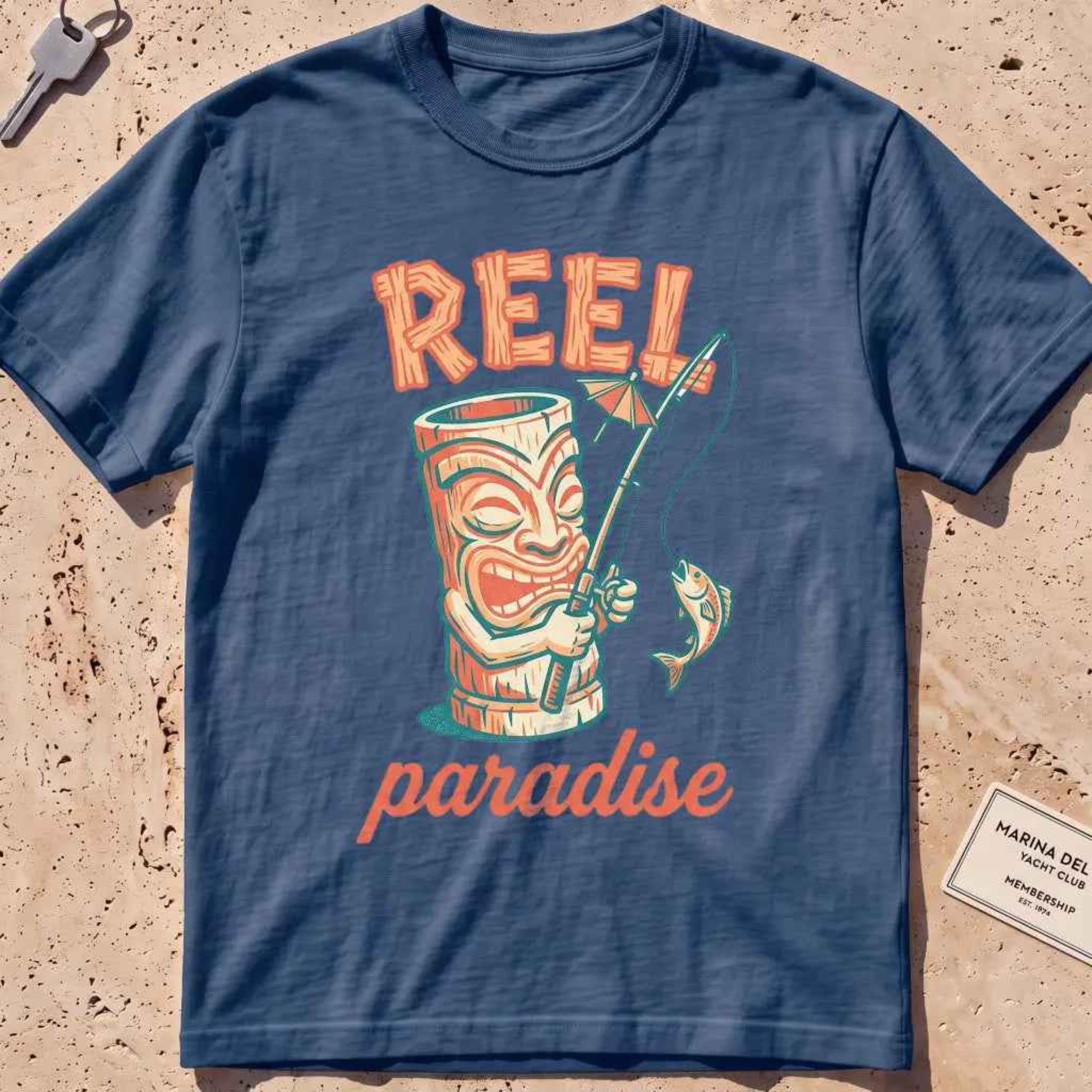 midnight heavyweight tee with a playful tiki mug and "Reel Paradise" text graphic.