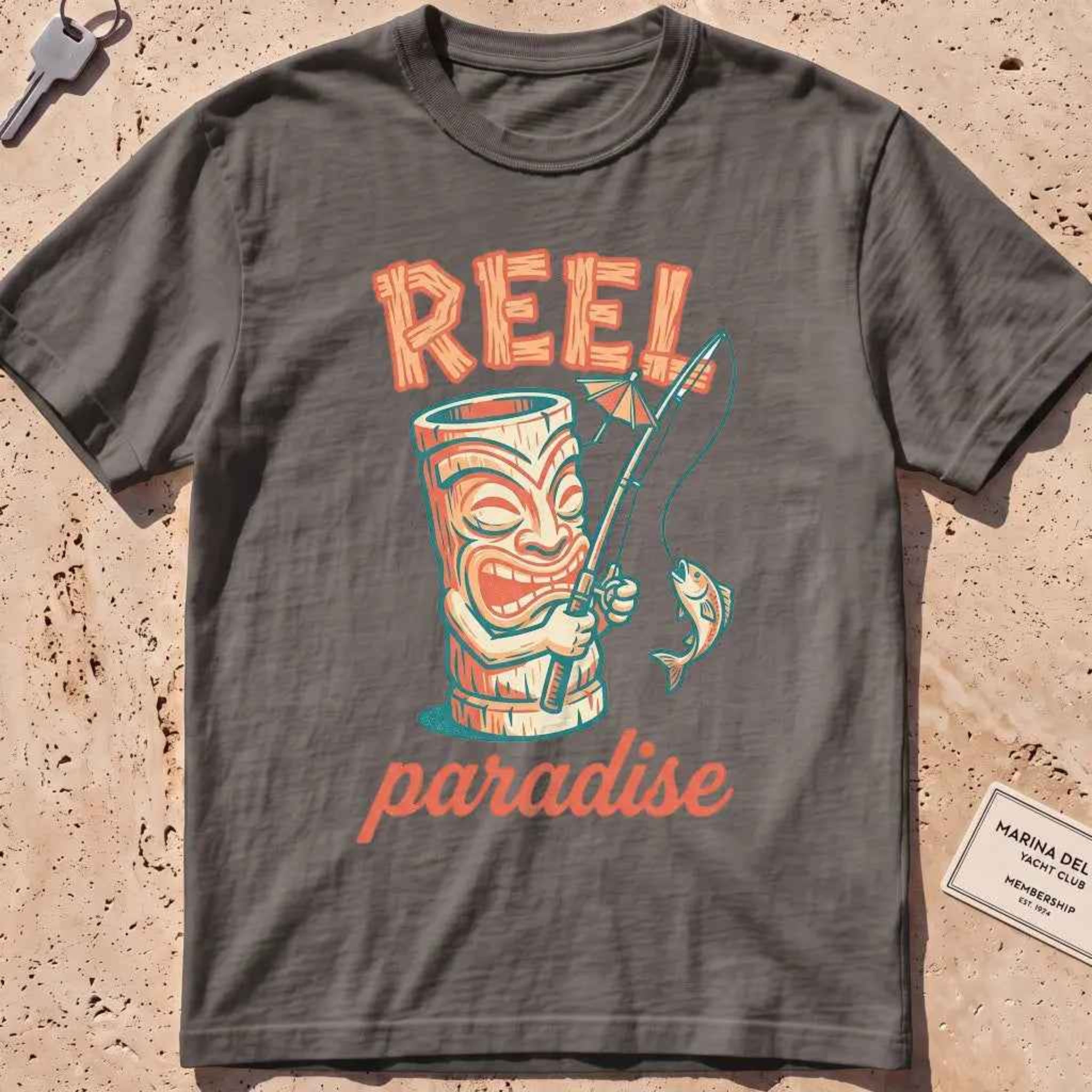 pepper heavyweight tee with a playful tiki mug and "Reel Paradise" text graphic.