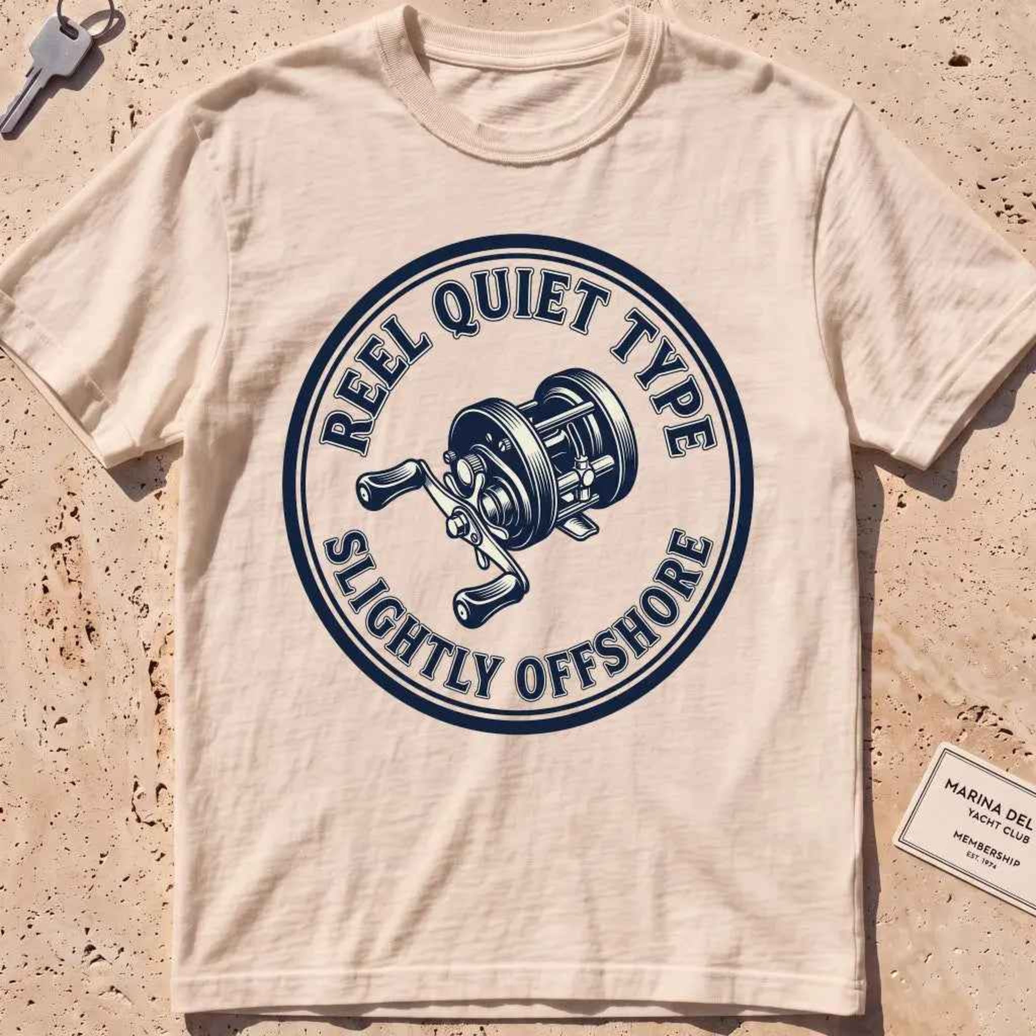 ivory heavyweight tee with an engraved fishing-reel "Reel Quiet Type" crest.