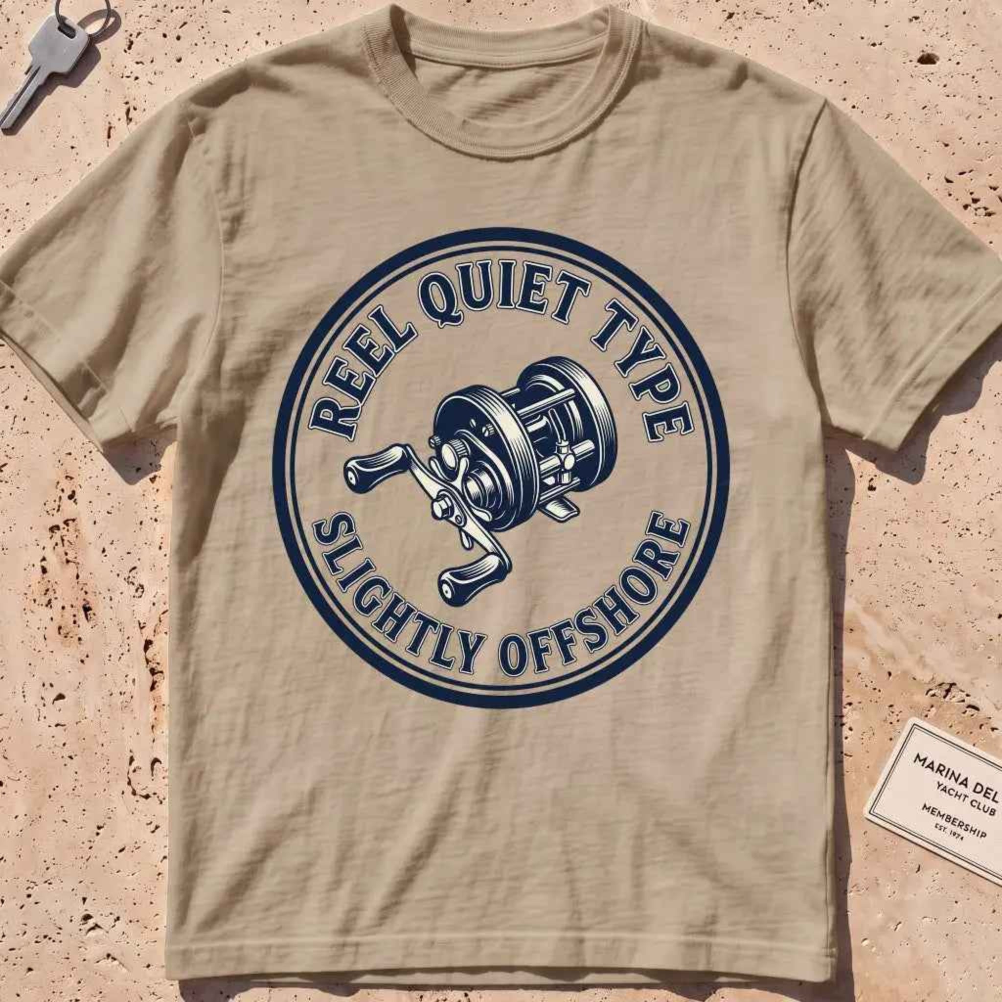 khaki heavyweight tee with an engraved fishing-reel "Reel Quiet Type" crest.