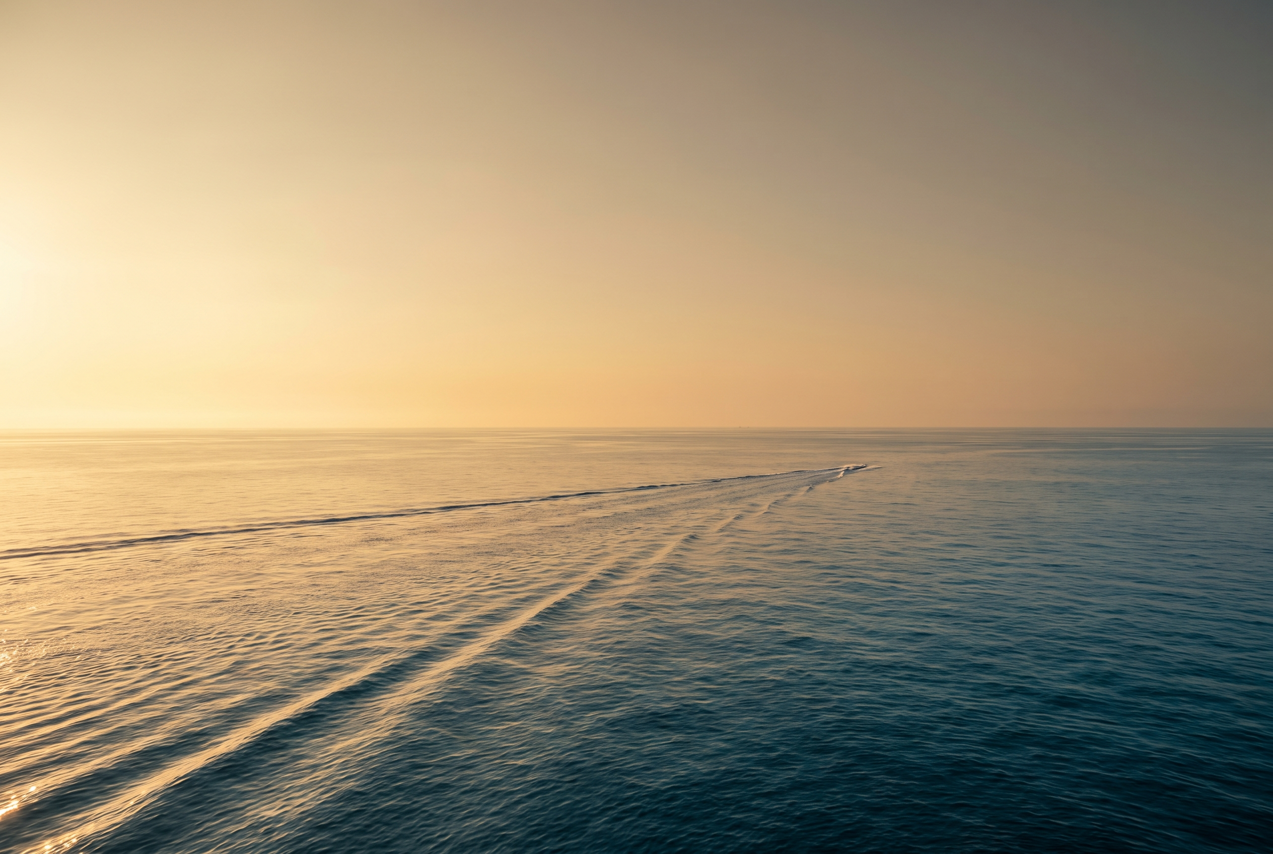 An empty wake trailing across calm open water at golden hour