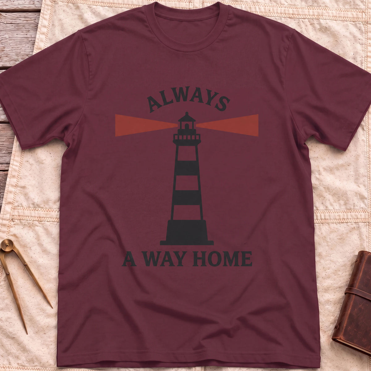 Front view of the maroon Always a Way Home T-Shirt with a striped lighthouse sending out red beams of light.