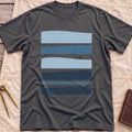 Front view of the dark heather Between Sets T-Shirt with layered bands of blue water and a small figure on a board between them.