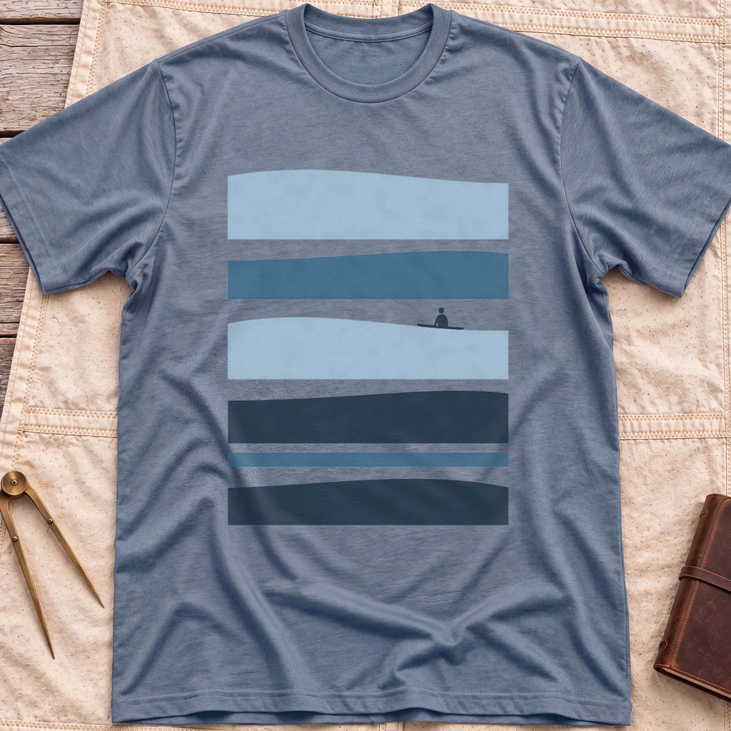 Front view of the heather indigo Between Sets T-Shirt with layered bands of blue water and a small figure on a board between them.
