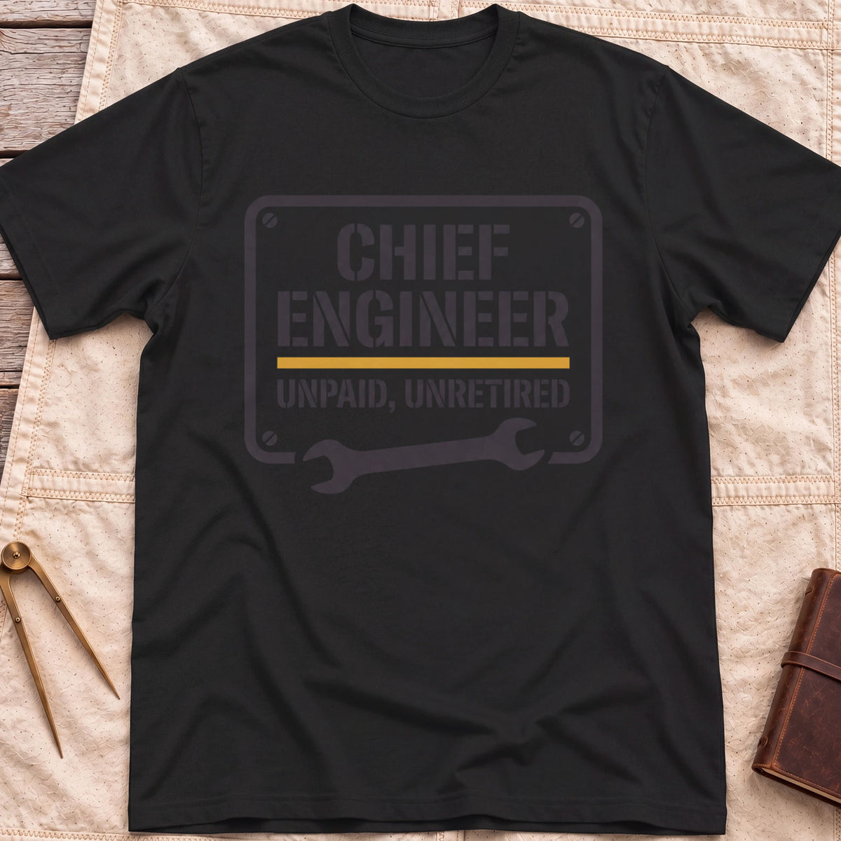 Front view of the black Chief Engineer T-Shirt with a stencil-style plate reading Unpaid, Unretired above a wrench.