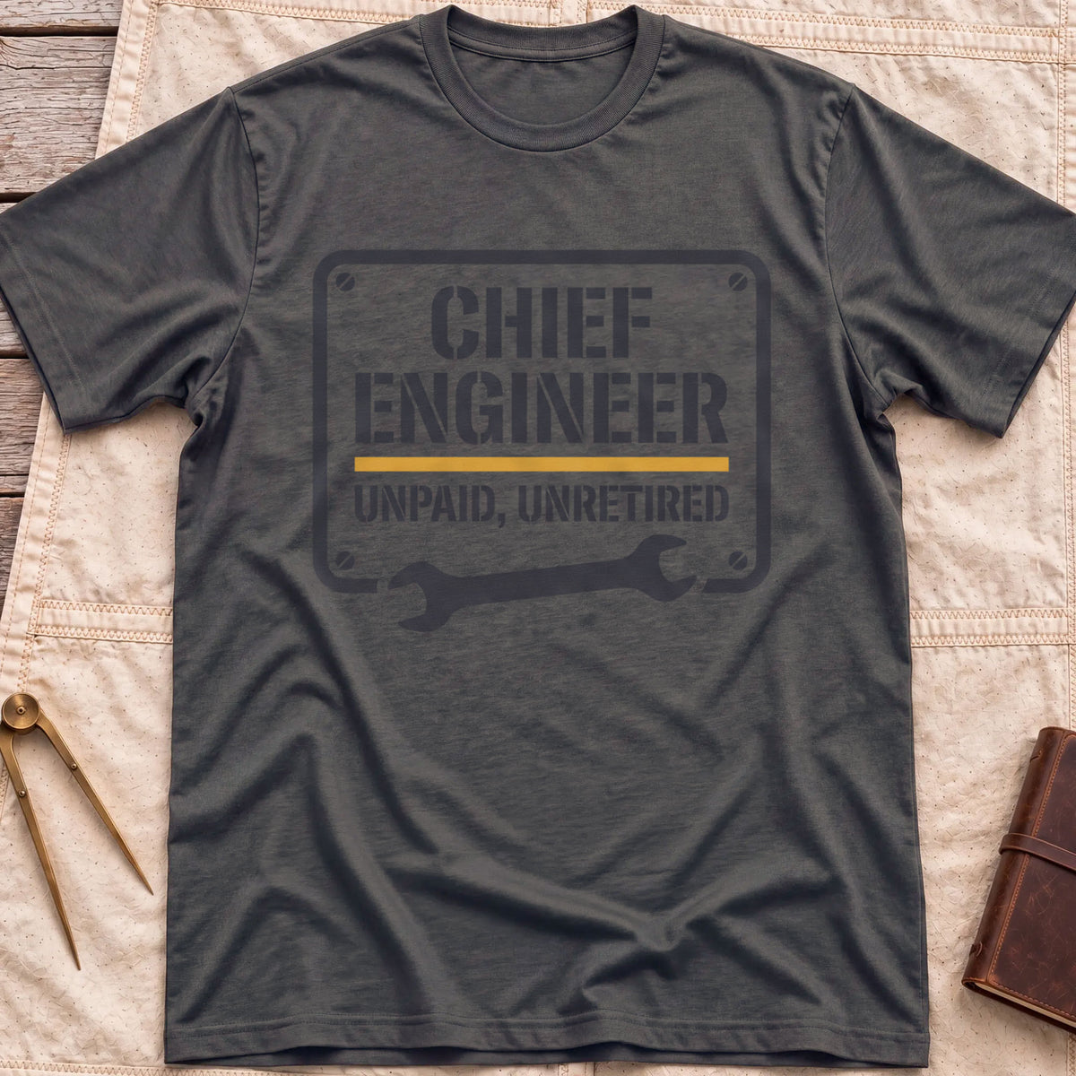 Front view of the dark heather Chief Engineer T-Shirt with a stencil-style plate reading Unpaid, Unretired above a wrench.