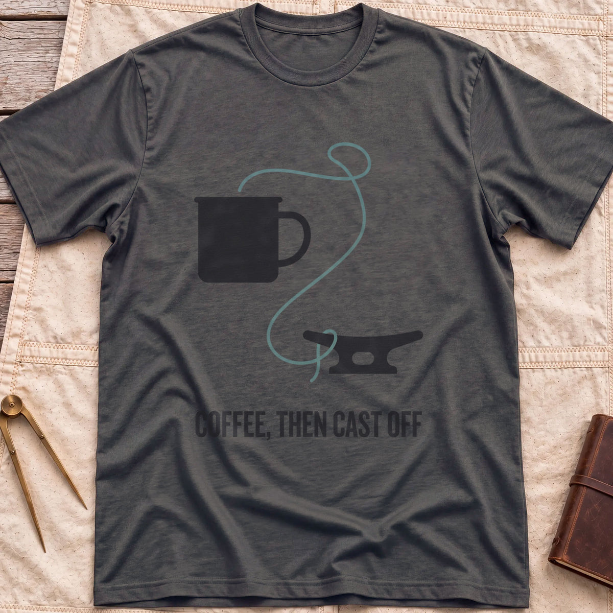 Front view of the dark heather Coffee Then Cast Off T-Shirt with a mug and a single line trailing from it to a dock cleat.