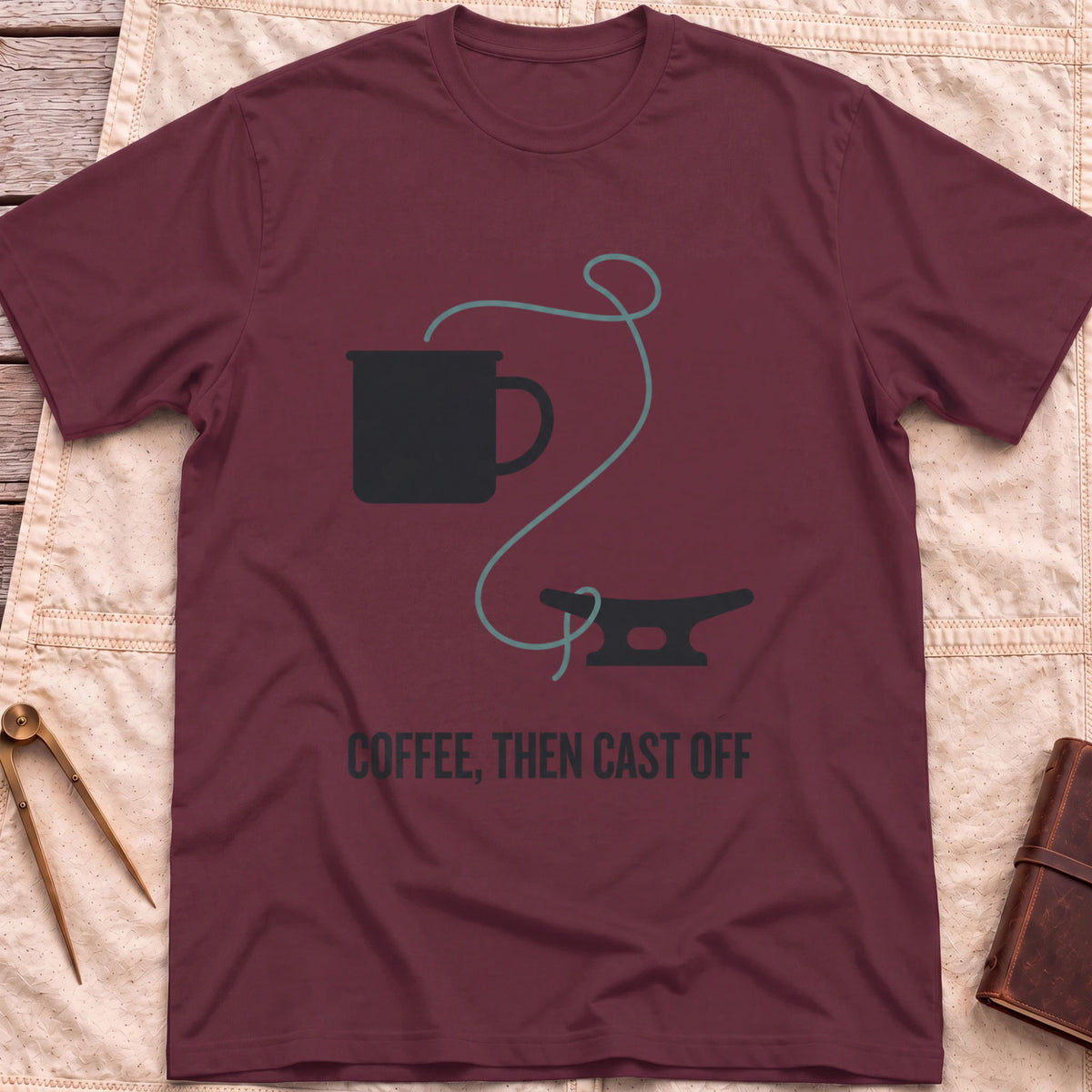 Front view of the maroon Coffee Then Cast Off T-Shirt with a mug and a single line trailing from it to a dock cleat.