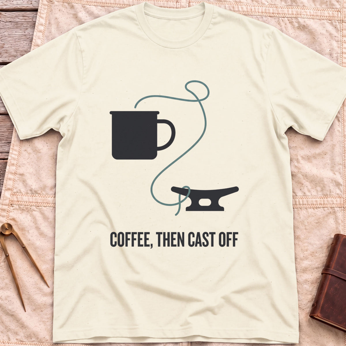 Front view of the natural Coffee Then Cast Off T-Shirt with a mug and a single line trailing from it to a dock cleat.