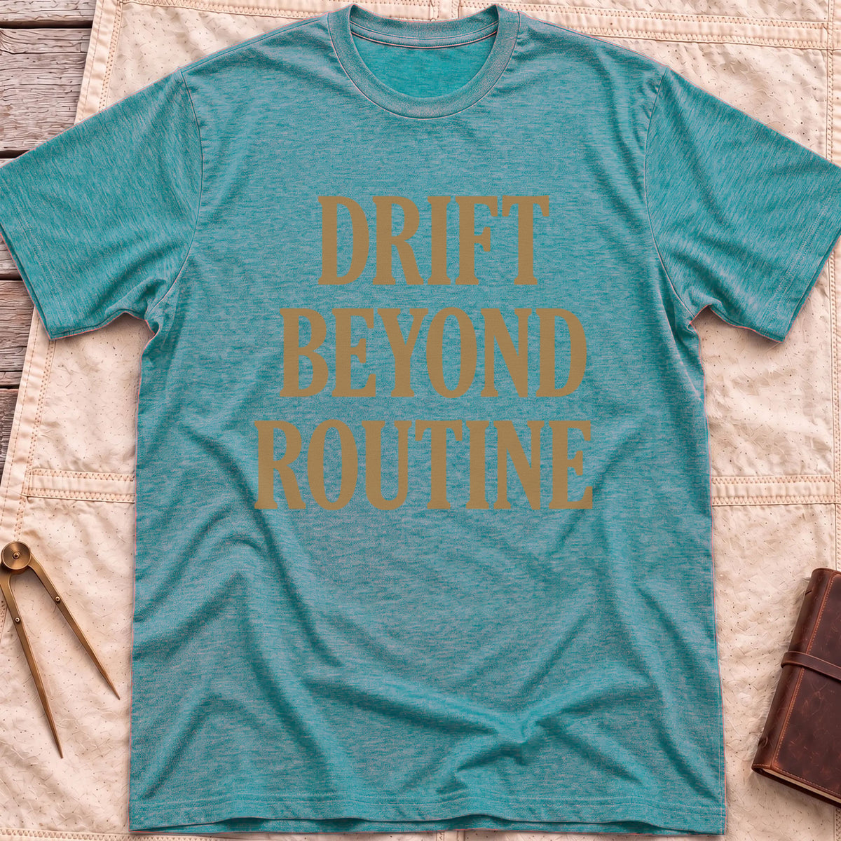 Front view of the heather galapagos blue Drift Beyond Routine T-Shirt with the words Drift Beyond Routine in large tan capitals.