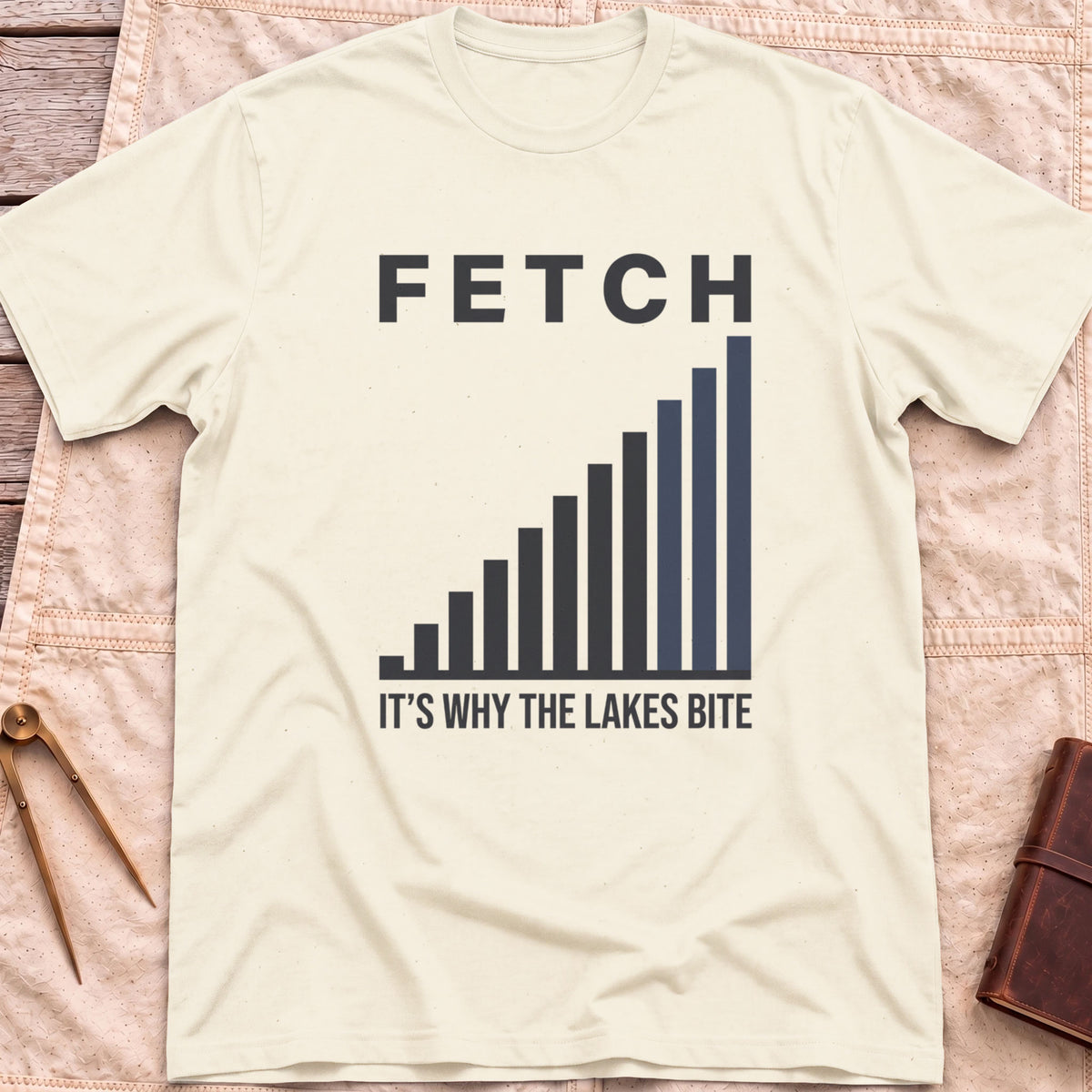 Front view of the natural Fetch T-Shirt with a rising bar chart and the words It's Why the Lakes Bite.