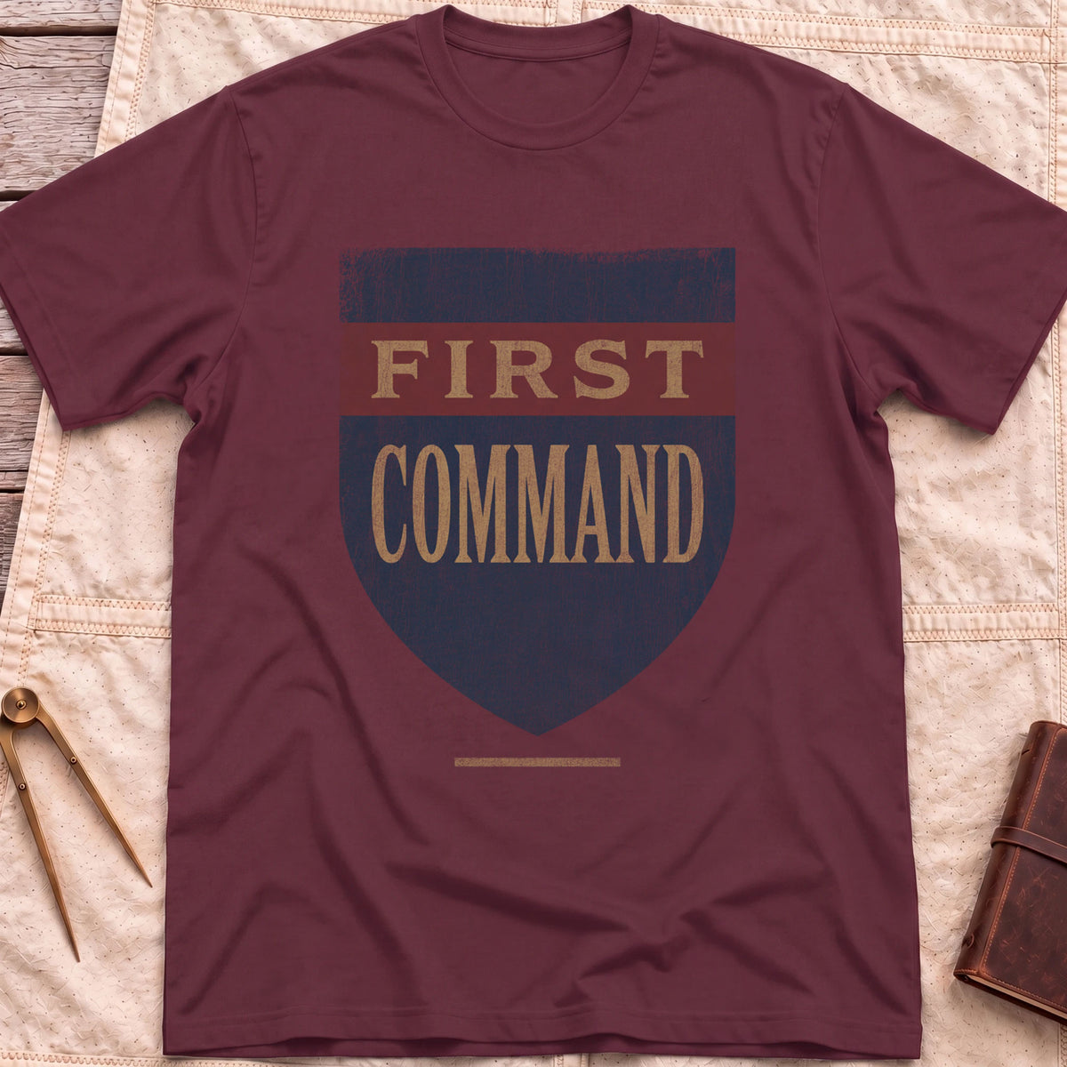 Front view of the maroon First Command T-Shirt with a distressed navy shield and a red band, lettered First Command.