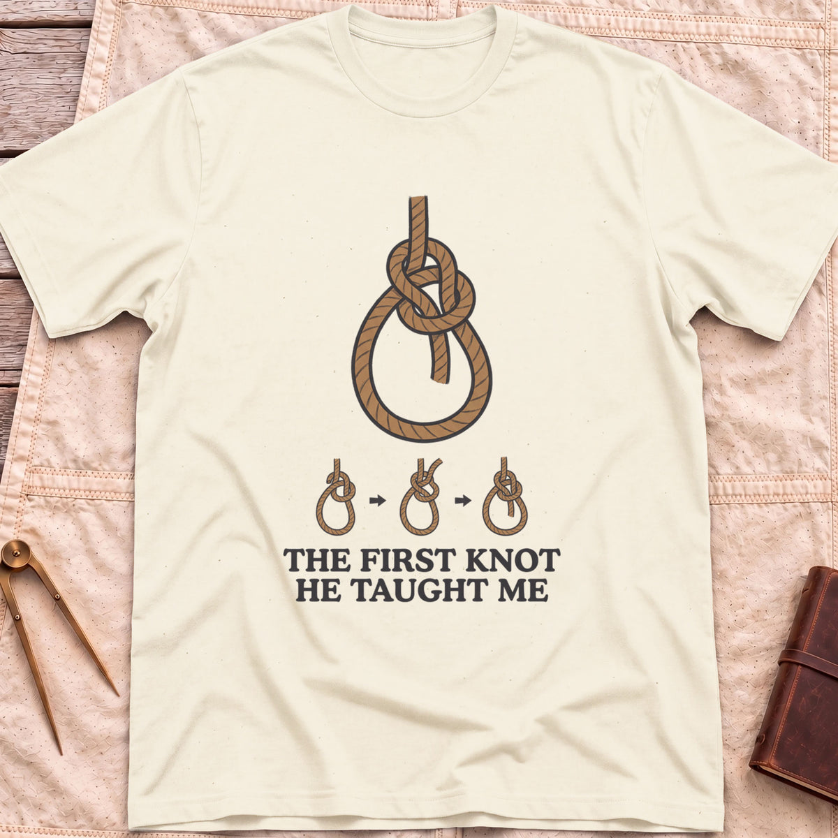 Front view of the natural First Knot He Taught Me T-Shirt with a large rope knot above three small diagrams showing it being tied.