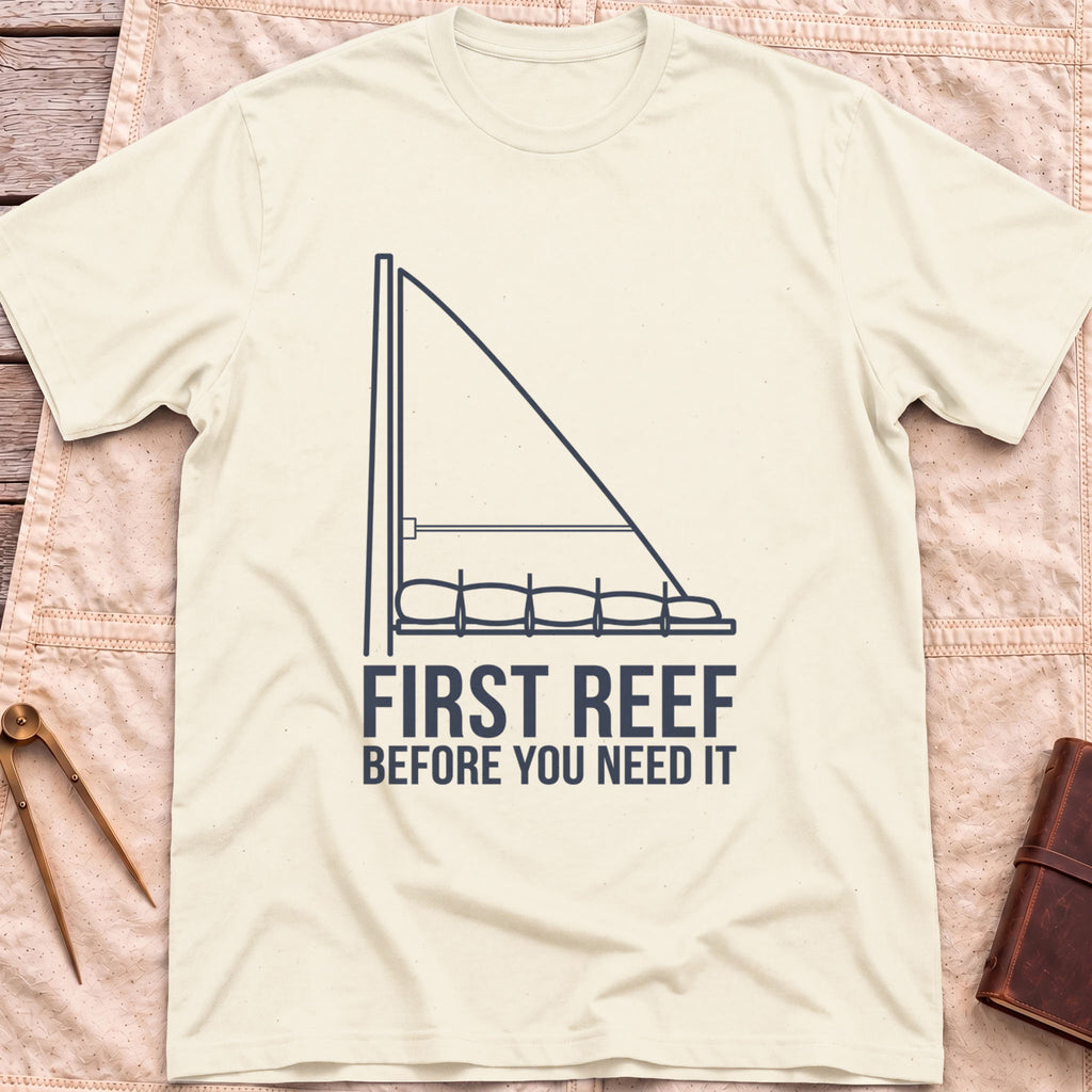 Front view of the natural First Reef T-Shirt with a line drawing of a sail with its lower section folded along the boom, above the words Before You Need It.