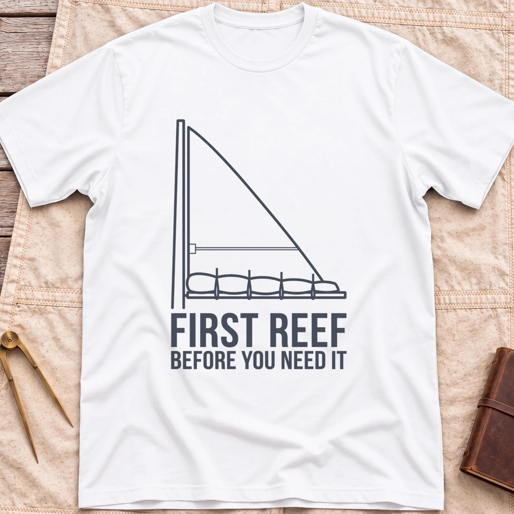 Front view of the white First Reef T-Shirt with a line drawing of a sail with its lower section folded along the boom, above the words Before You Need It.