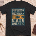 Front view of the black Five Lakes T-Shirt with a distressed panel listing Superior, Michigan, Huron, Erie and Ontario, with Huron highlighted.