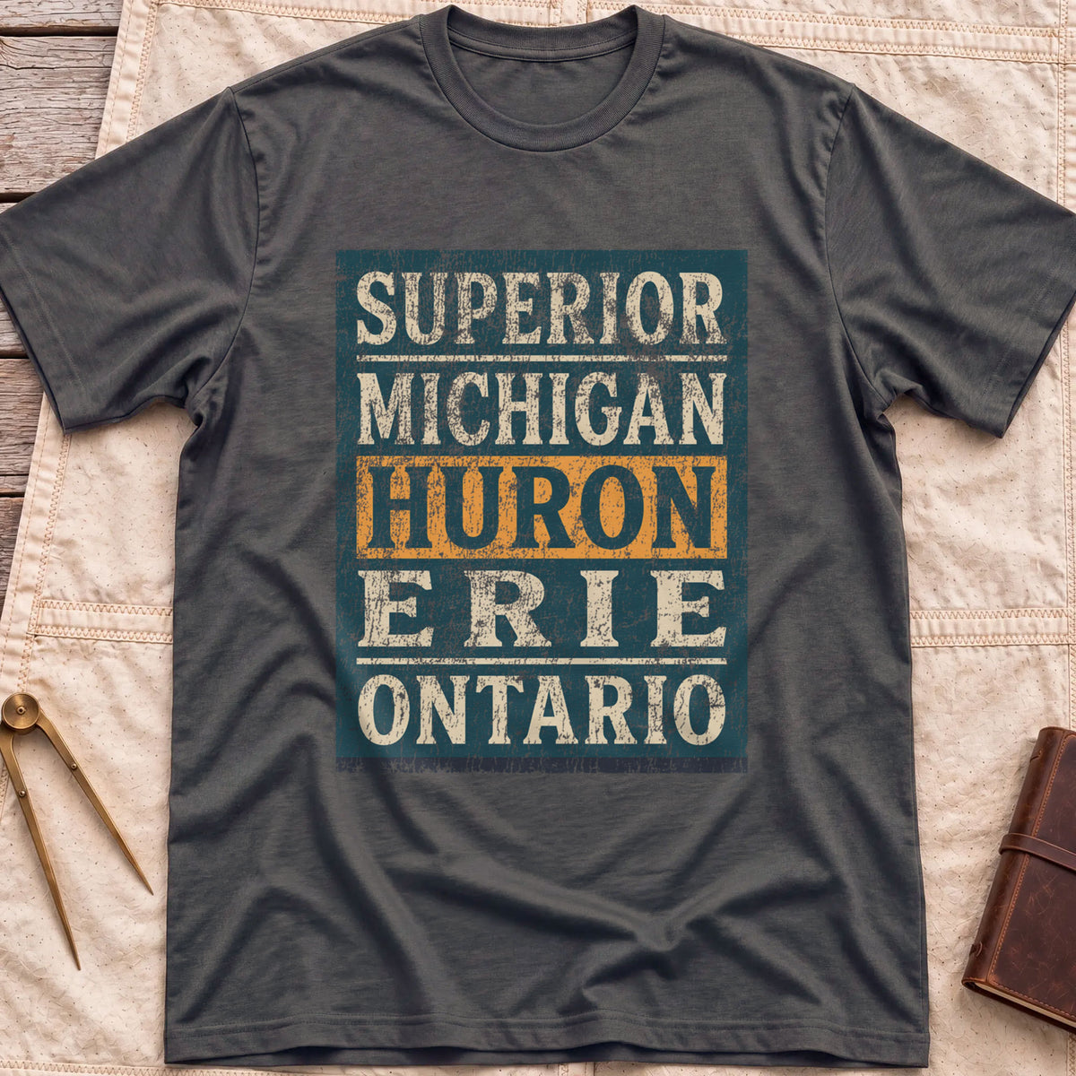 Front view of the dark heather Five Lakes T-Shirt with a distressed panel listing Superior, Michigan, Huron, Erie and Ontario, with Huron highlighted.