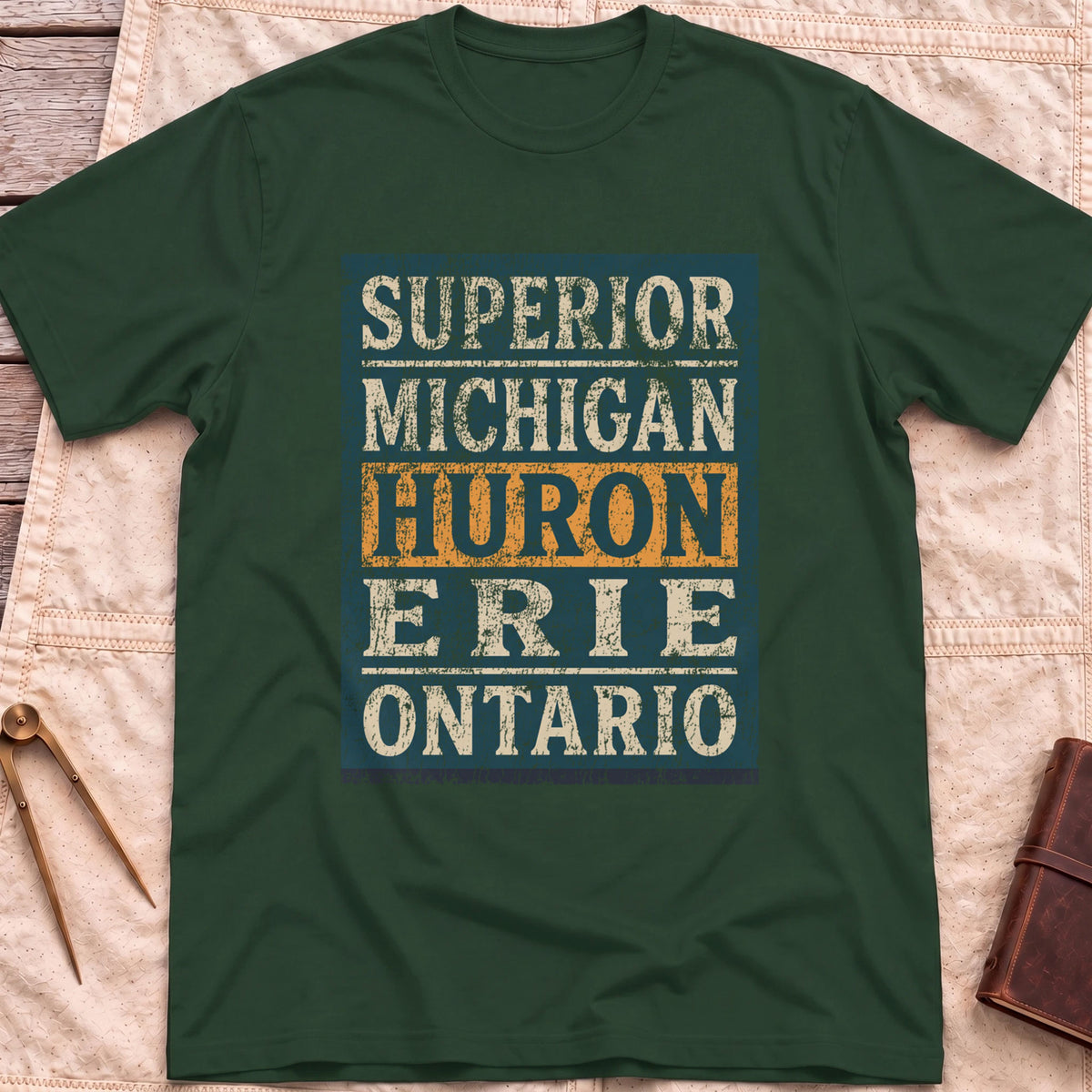 Front view of the forest green Five Lakes T-Shirt with a distressed panel listing Superior, Michigan, Huron, Erie and Ontario, with Huron highlighted.