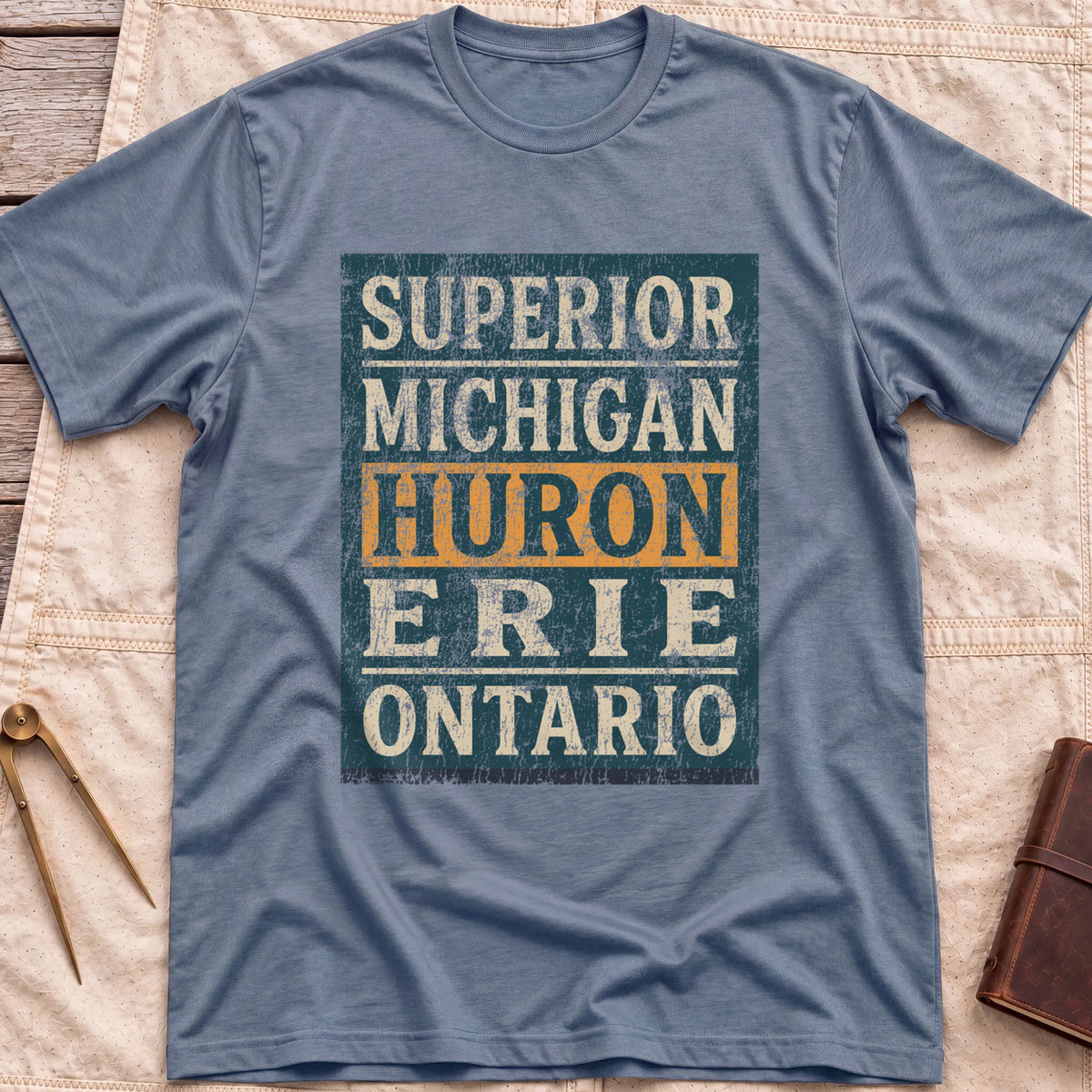 Front view of the heather indigo Five Lakes T-Shirt with a distressed panel listing Superior, Michigan, Huron, Erie and Ontario, with Huron highlighted.