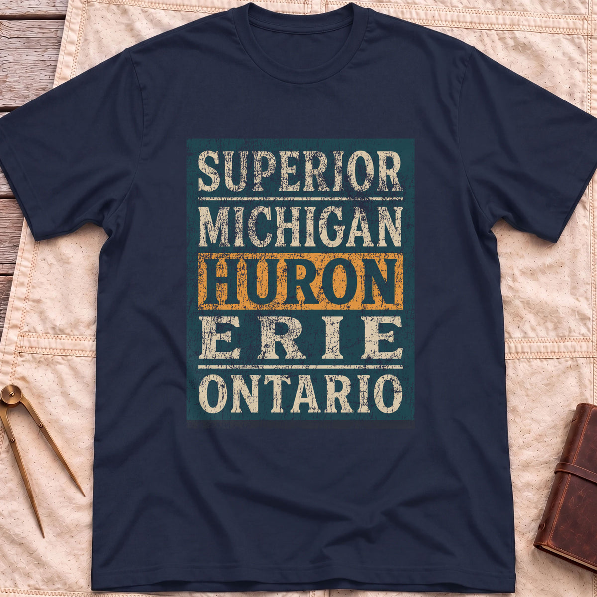 Front view of the navy Five Lakes T-Shirt with a distressed panel listing Superior, Michigan, Huron, Erie and Ontario, with Huron highlighted.