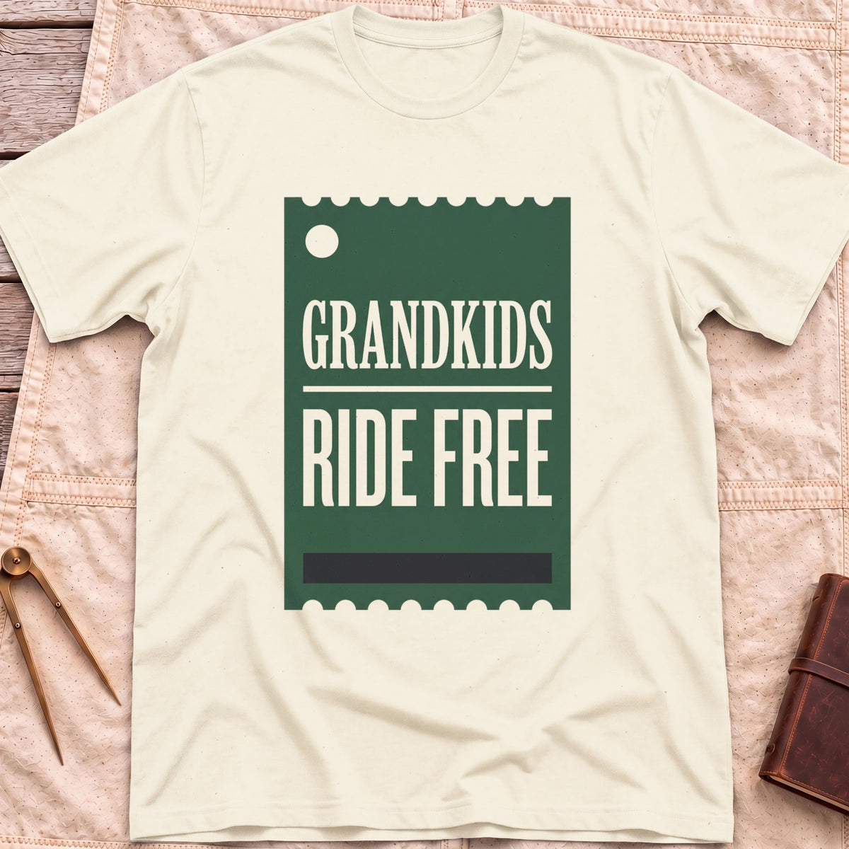 Front view of the natural Grandkids Ride Free T-Shirt with a green ticket-shaped graphic reading Grandkids Ride Free.