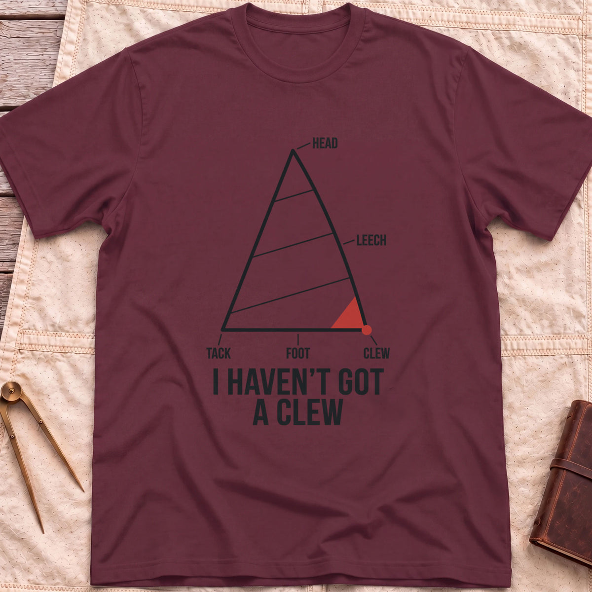 Front view of the maroon I Haven't Got A Clew T-Shirt with a labelled sail diagram, the clew corner marked in red.