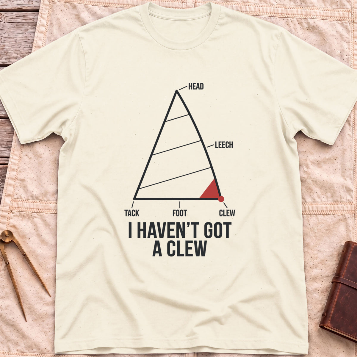 Front view of the natural I Haven't Got A Clew T-Shirt with a labelled sail diagram, the clew corner marked in red.