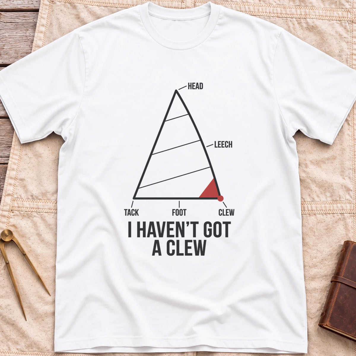 Front view of the white I Haven't Got A Clew T-Shirt with a labelled sail diagram, the clew corner marked in red.