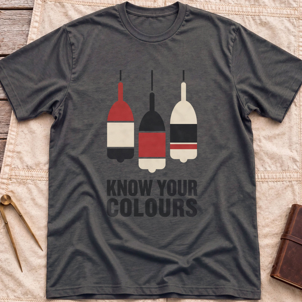 Front view of the dark heather Know Your Colours T-Shirt with three hanging buoys painted in red, black and cream bands above the words Know Your Colours.