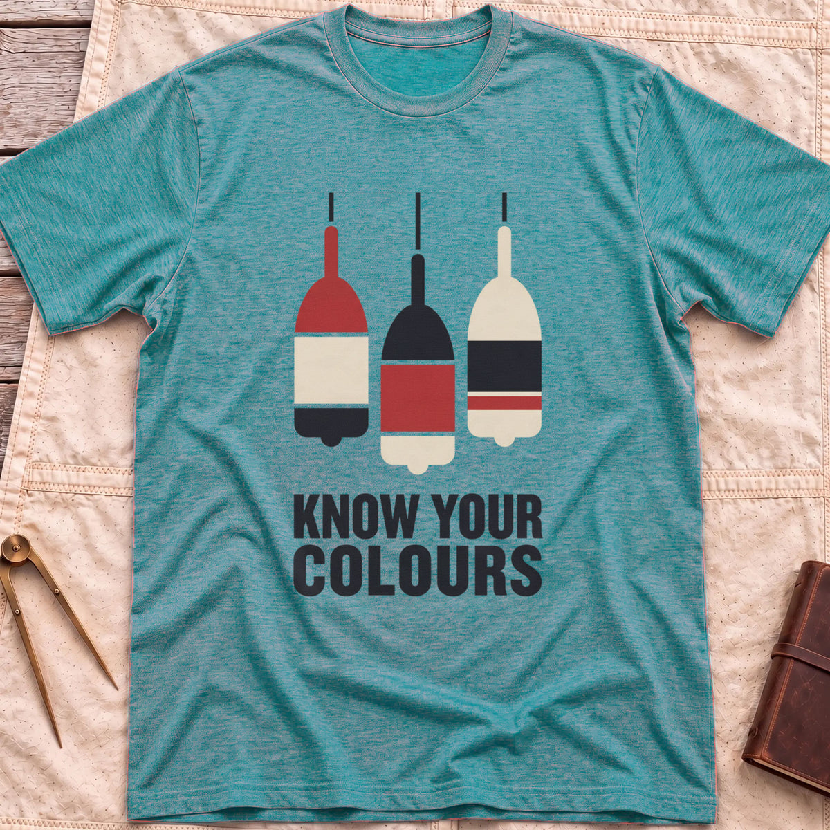 Front view of the heather galapagos blue Know Your Colours T-Shirt with three hanging buoys painted in red, black and cream bands above the words Know Your Colours.