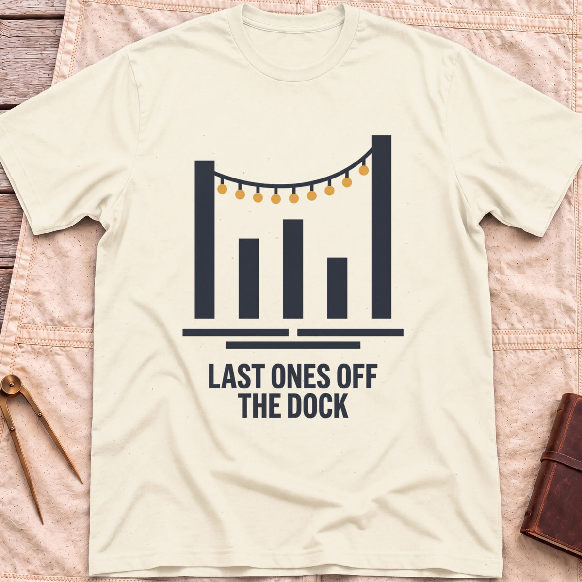 Front view of the natural Last Ones Off the Dock T-Shirt with a string of lights hung between tall dock posts.