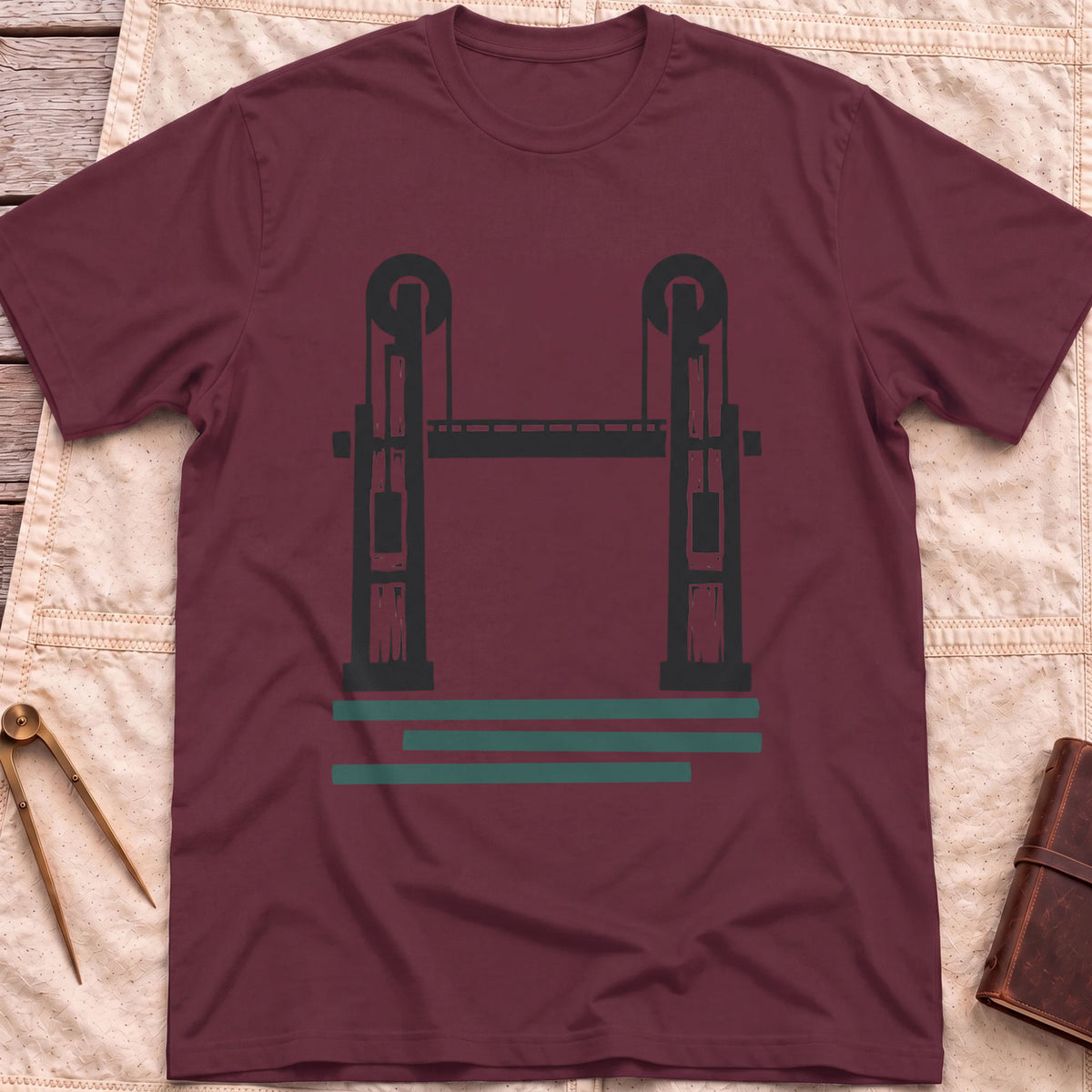 Front view of the maroon Lift Bridge T-Shirt with a silhouette of a lift bridge, its two towers topped with wheels.