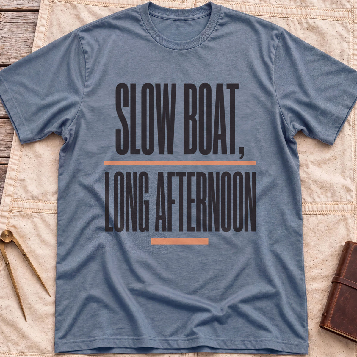 Front view of the heather indigo Long Afternoon T-Shirt with the words Slow Boat, Long Afternoon in tall condensed capitals between coral rules.