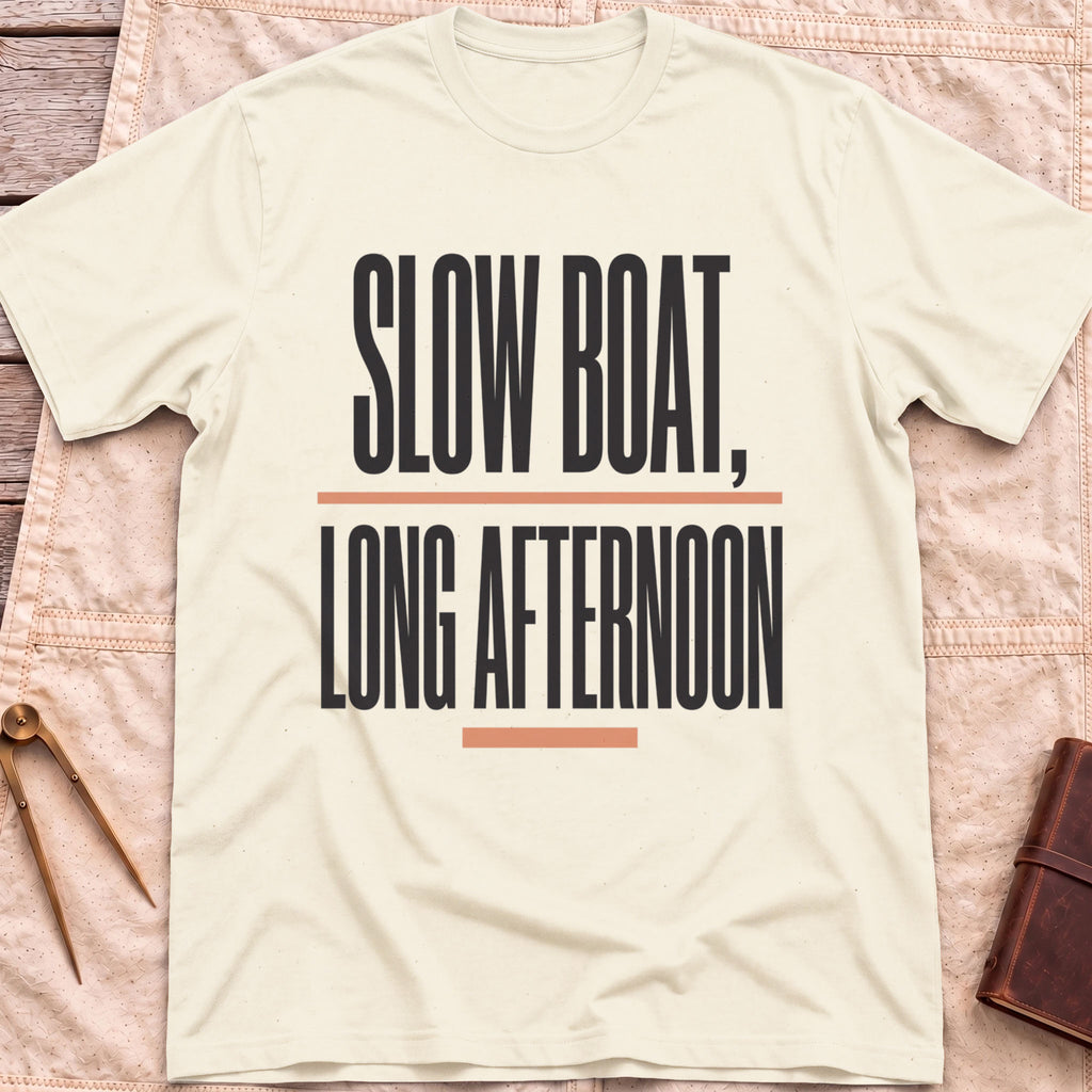 Front view of the natural Long Afternoon T-Shirt with the words Slow Boat, Long Afternoon in tall condensed capitals between coral rules.