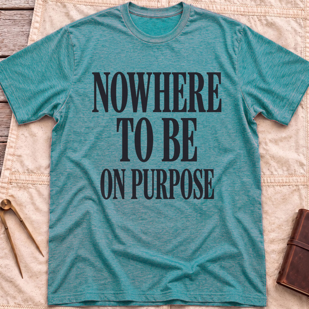 Front view of the heather galapagos blue Nowhere to Be T-Shirt with the words Nowhere to Be, On Purpose in tall condensed capitals.