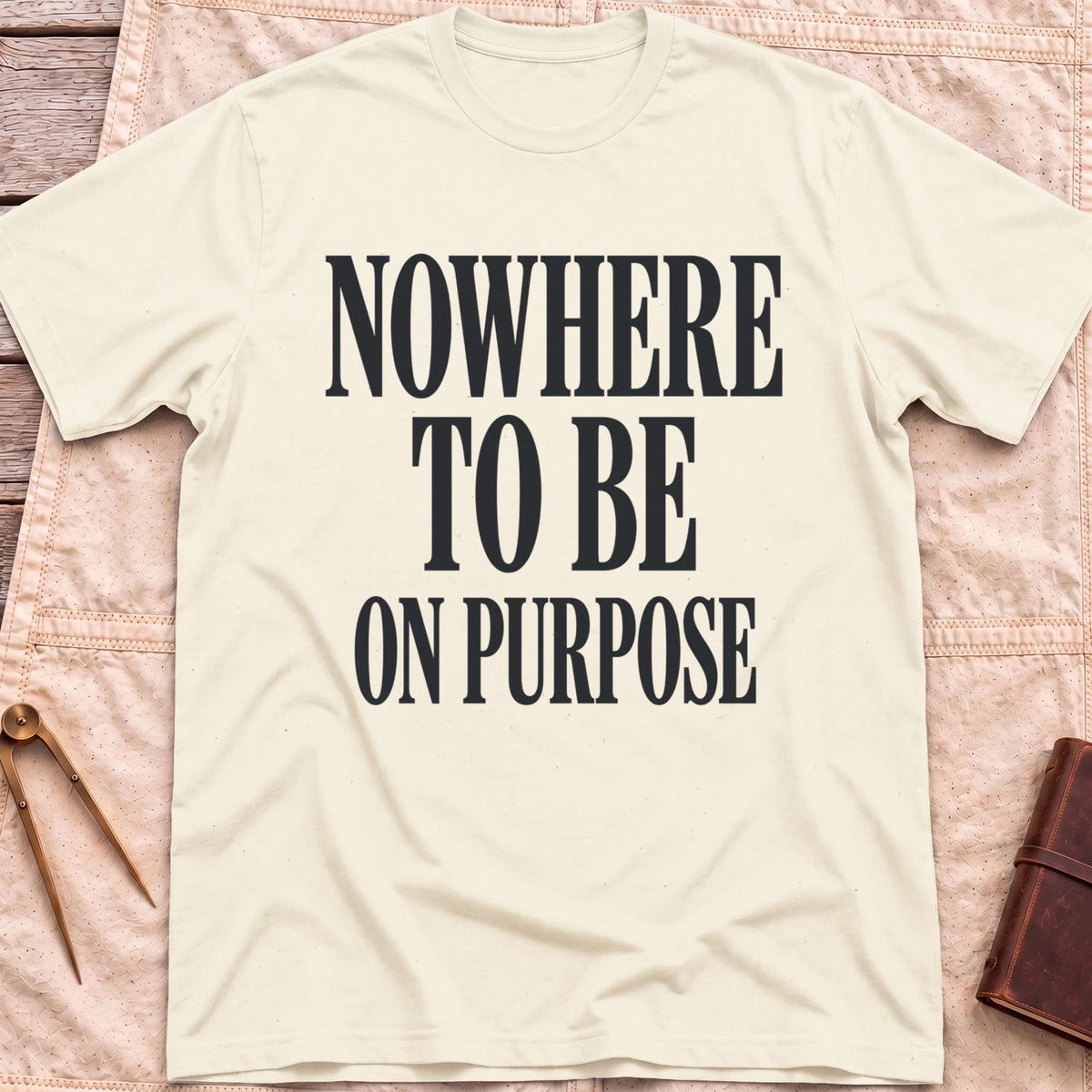 Front view of the natural Nowhere to Be T-Shirt with the words Nowhere to Be, On Purpose in tall condensed capitals.