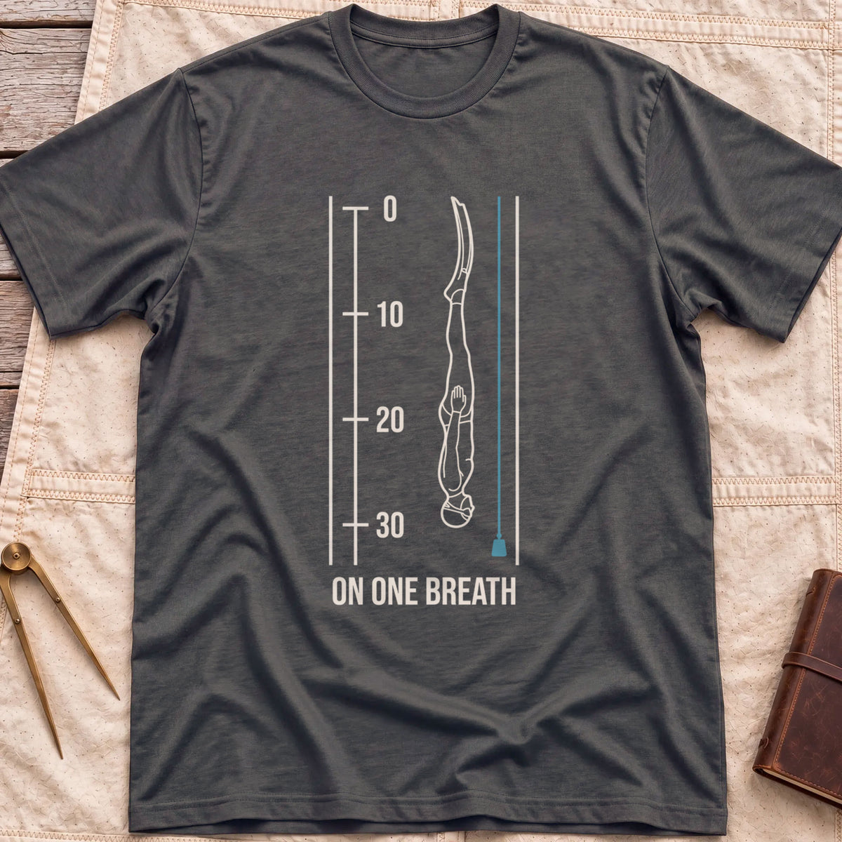 Front view of the dark heather On One Breath T-Shirt with a diver descending headfirst beside a depth scale from 0 to 30, above the words On One Breath.