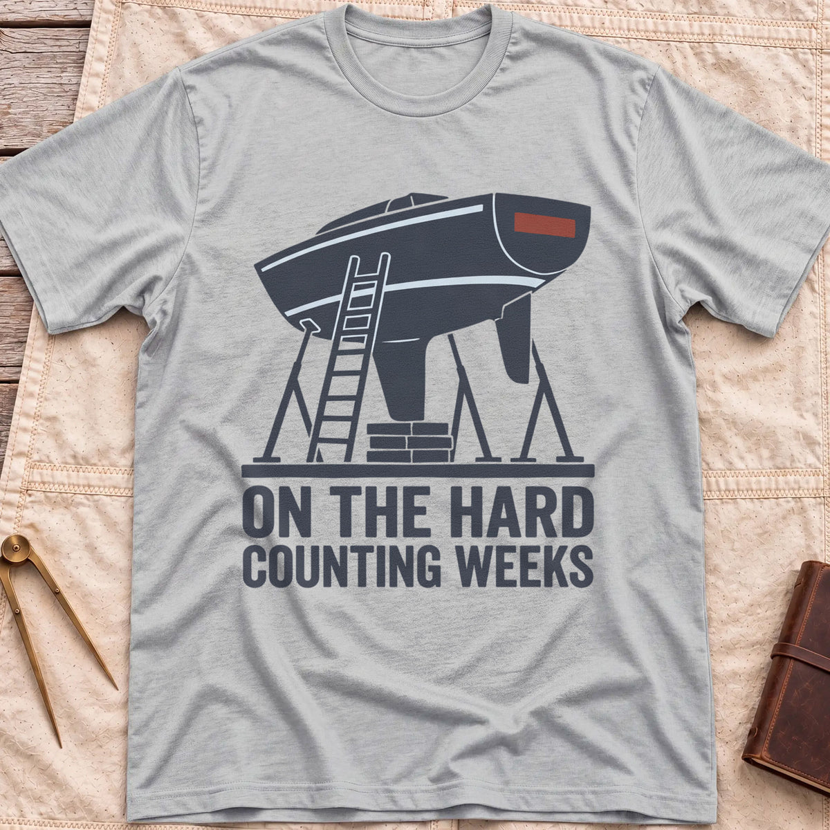 Front view of the sport grey On the Hard T-Shirt with a boat hull up on stands with a ladder against it, above the words Counting Weeks.