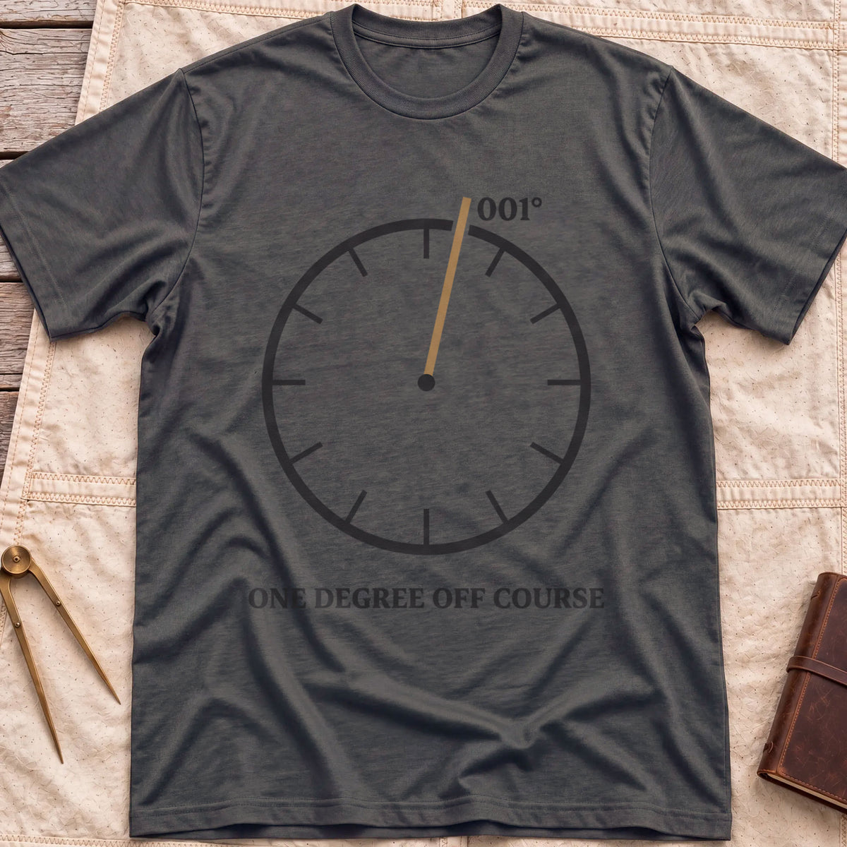 Front view of the dark heather One Degree Off Course T-Shirt with a round dial and a tan needle pointing to 001°.